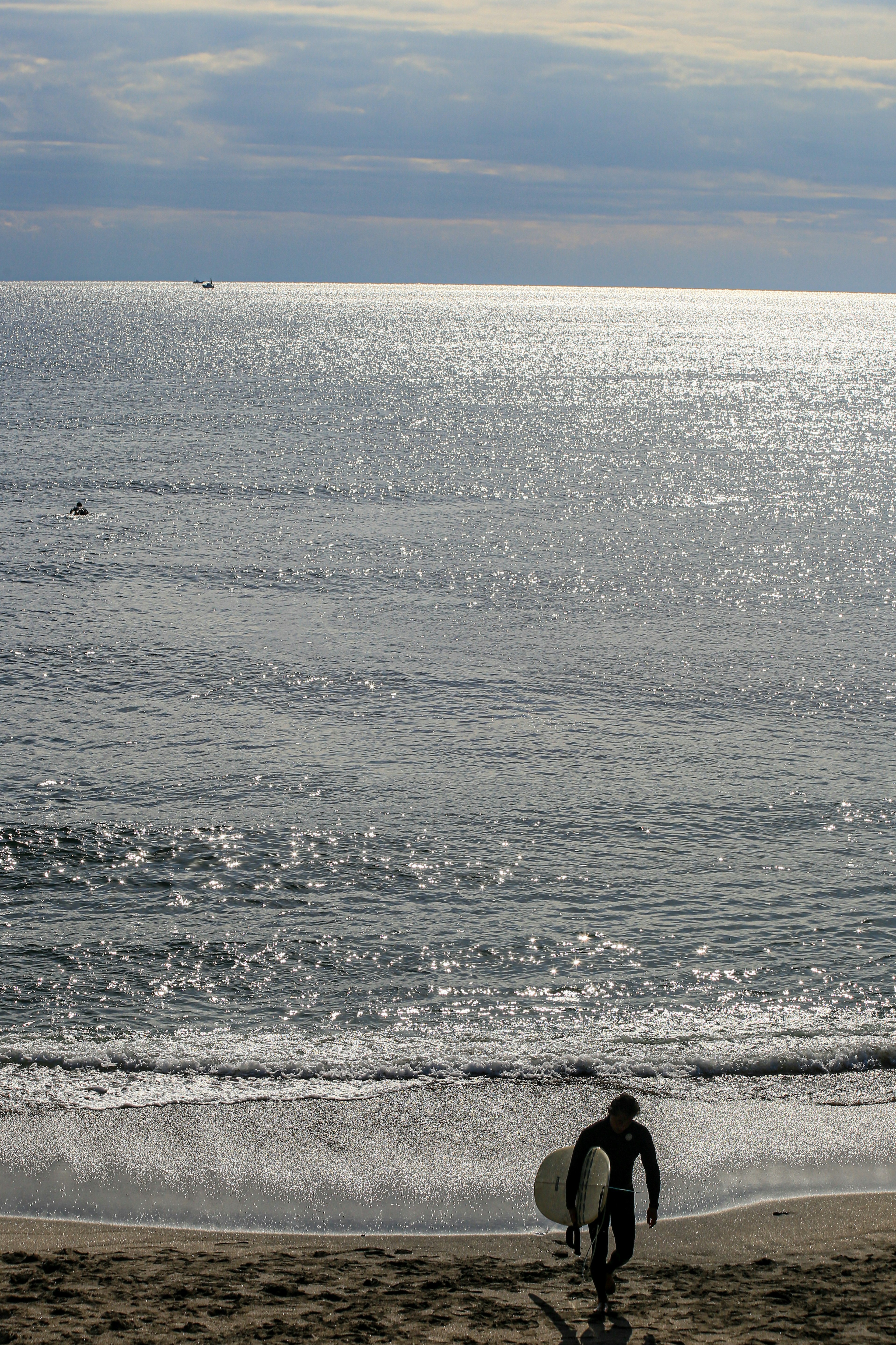 Silhouette of a person holding a surfboard by the beach