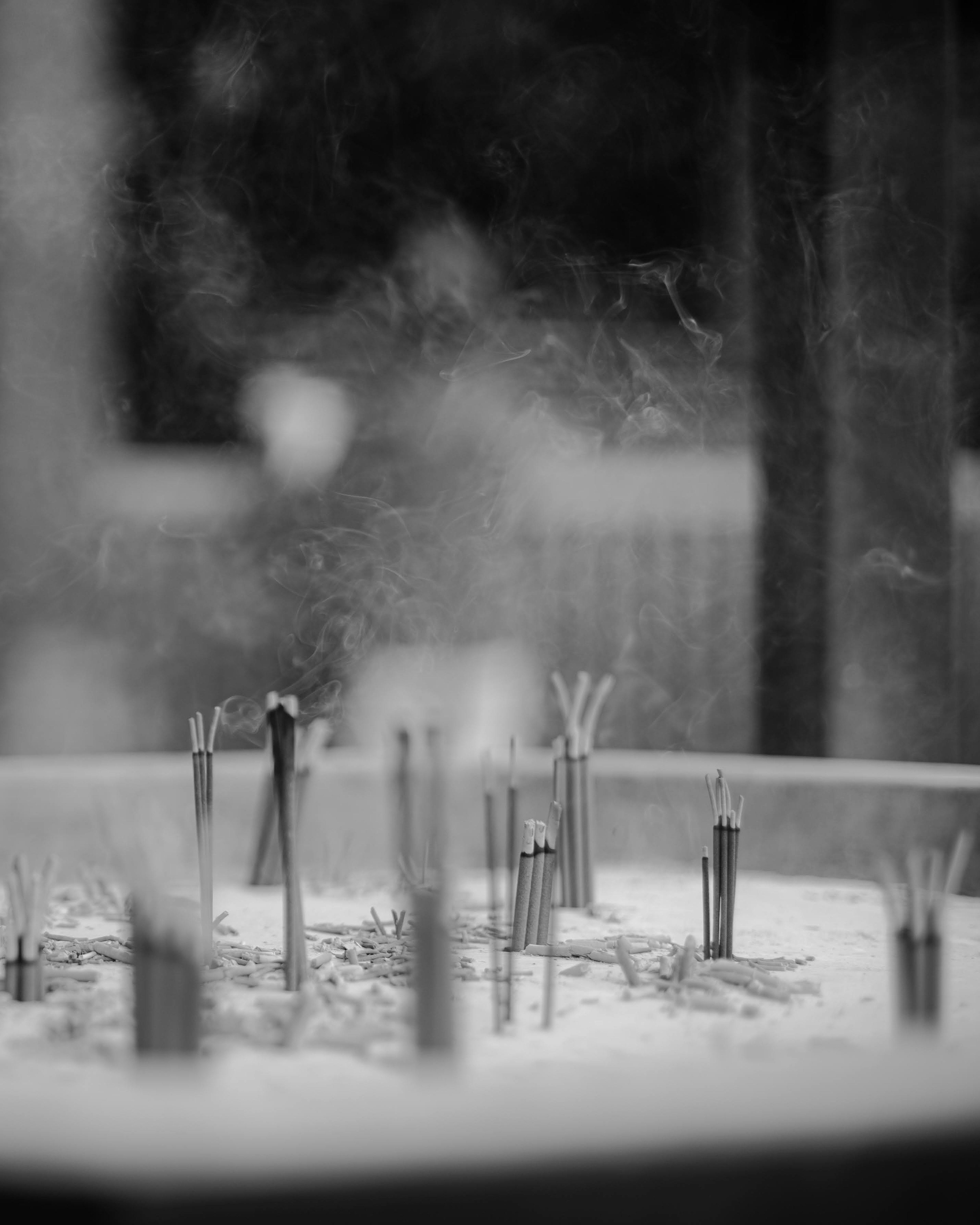 Close-up of incense sticks with rising smoke in black and white