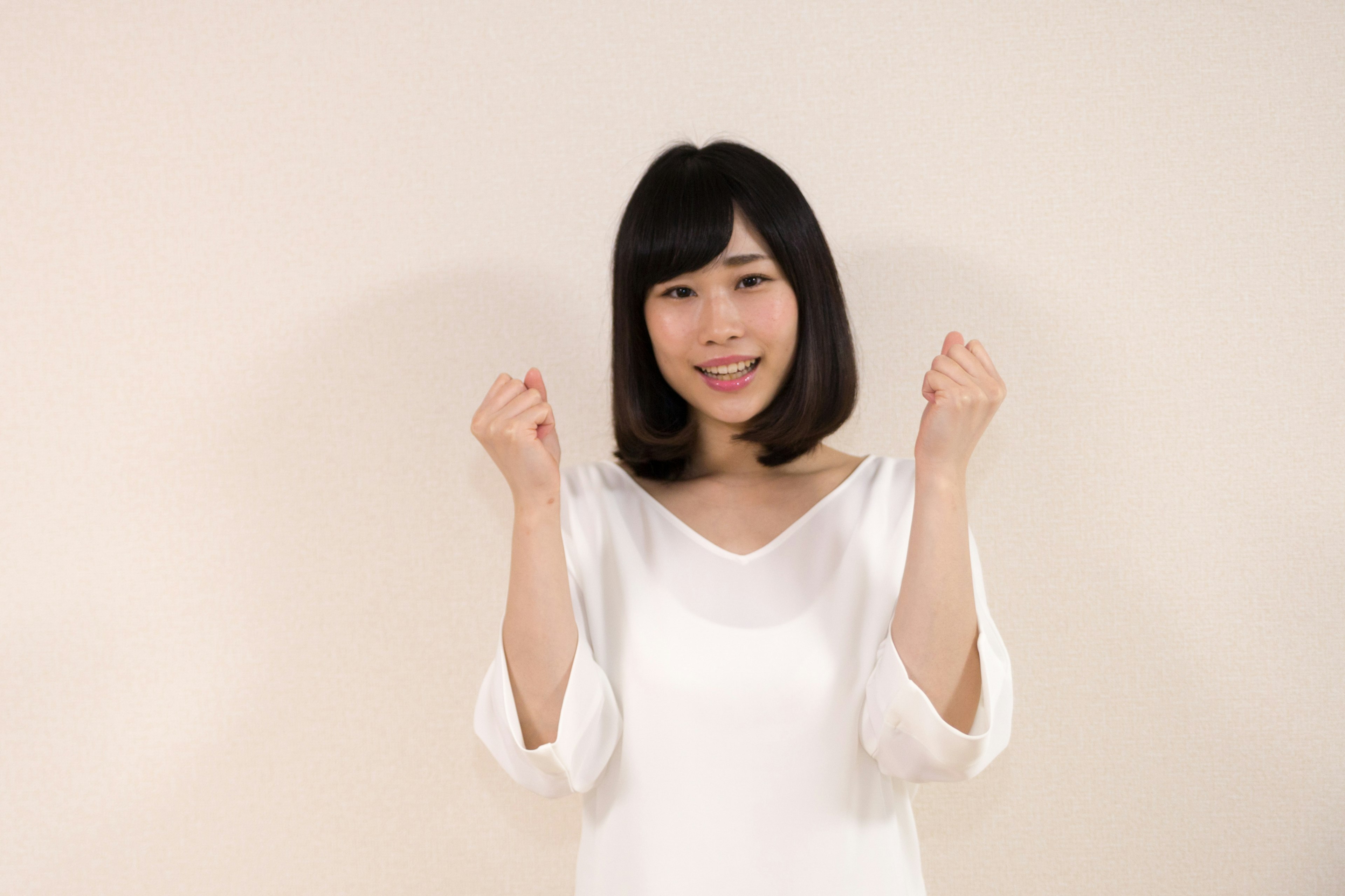 A woman in a white shirt is smiling and posing with her hands raised