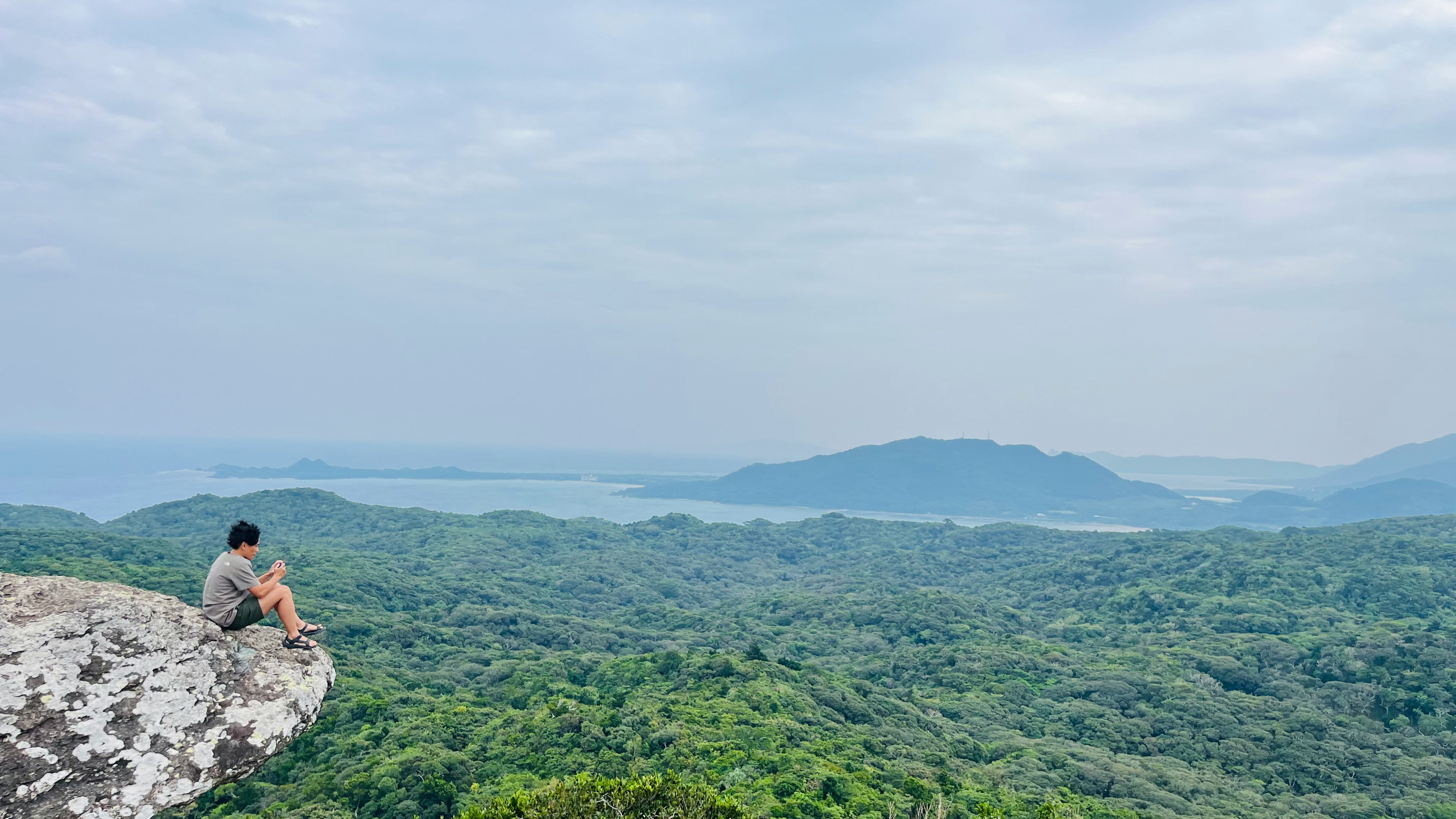 A man sitting on a rock overlooking lush green hills and the ocean