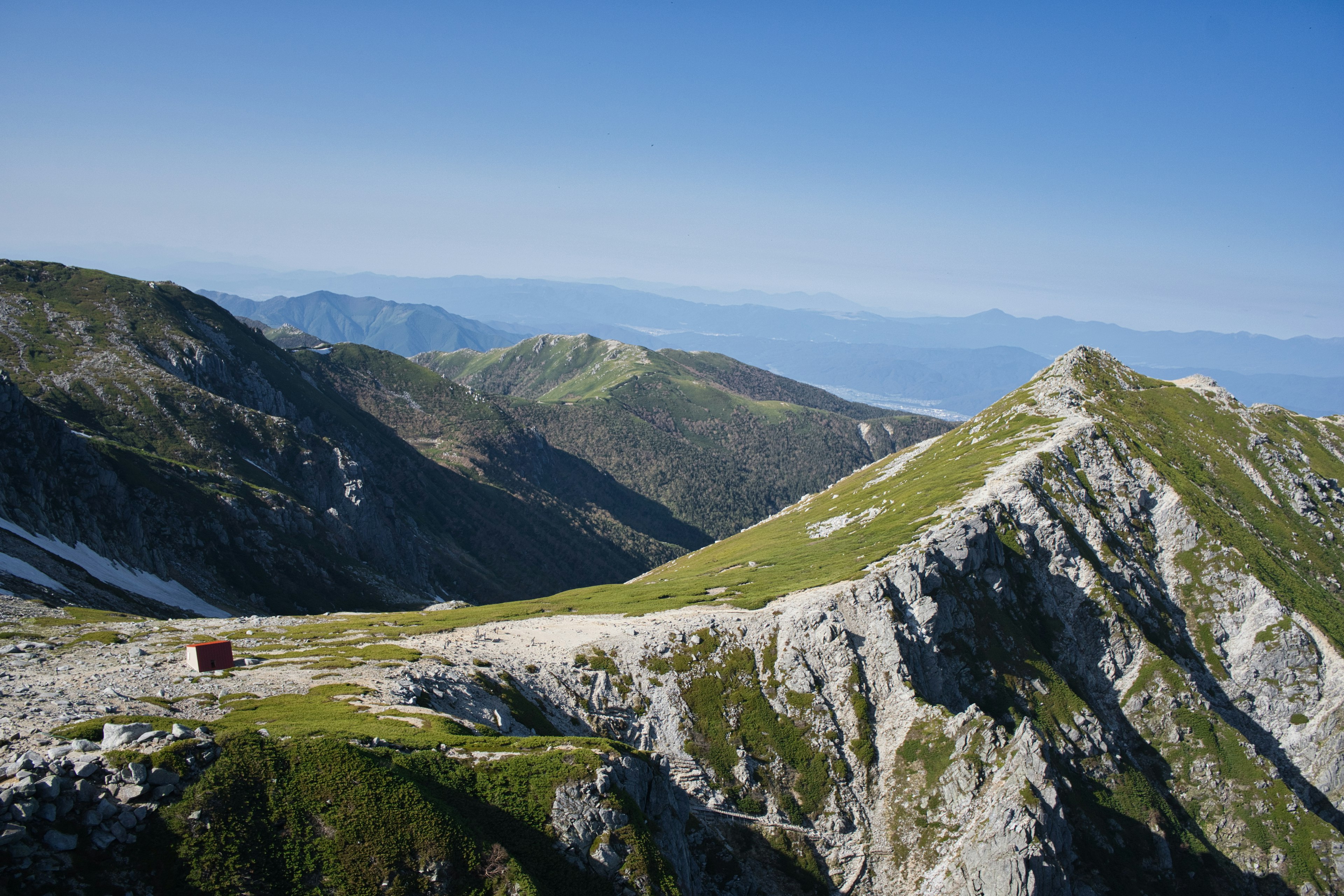 高山の緑の丘と岩の風景、青空と遠くの山々が見える