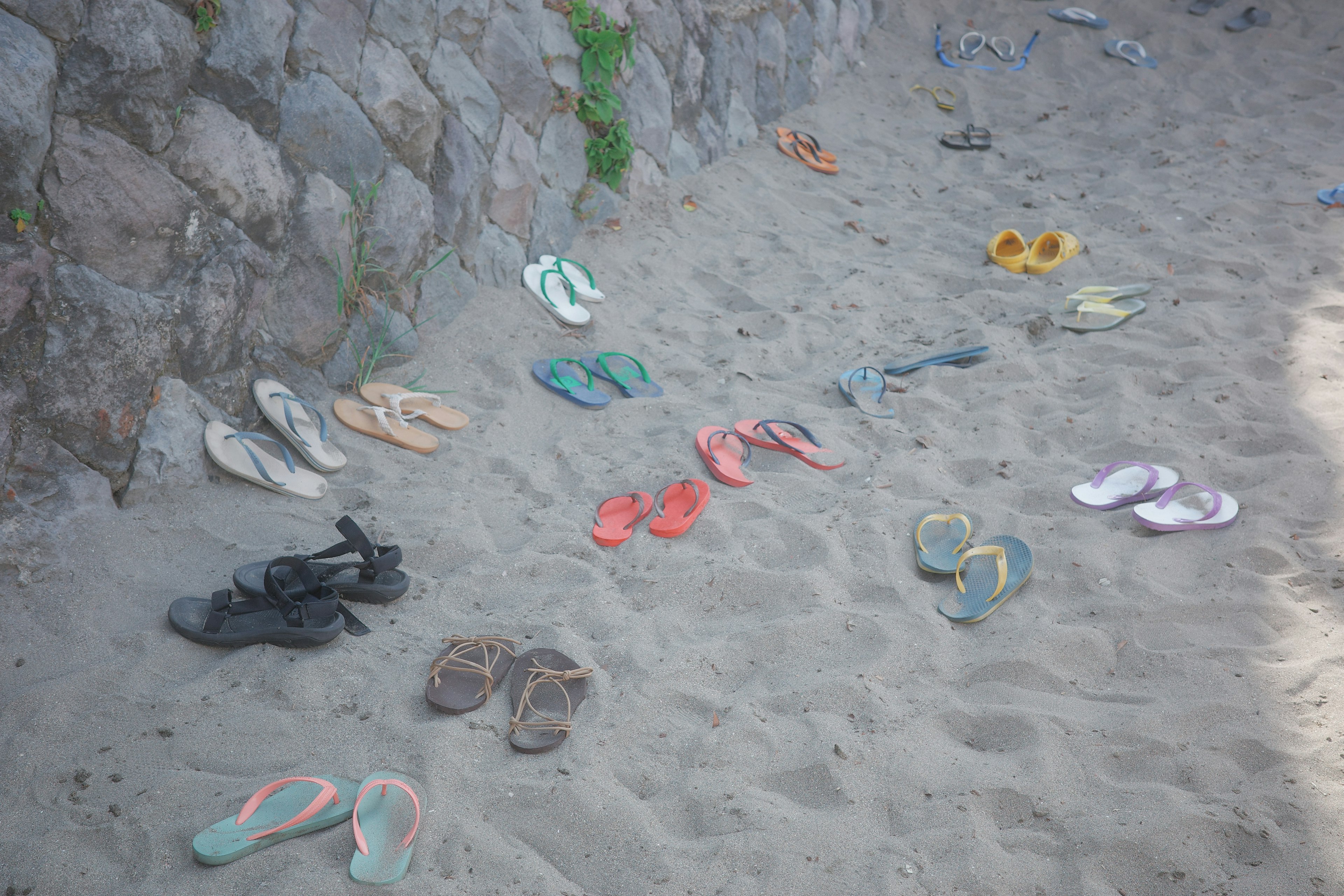 Varias sandalias y chanclas esparcidas en la playa de arena