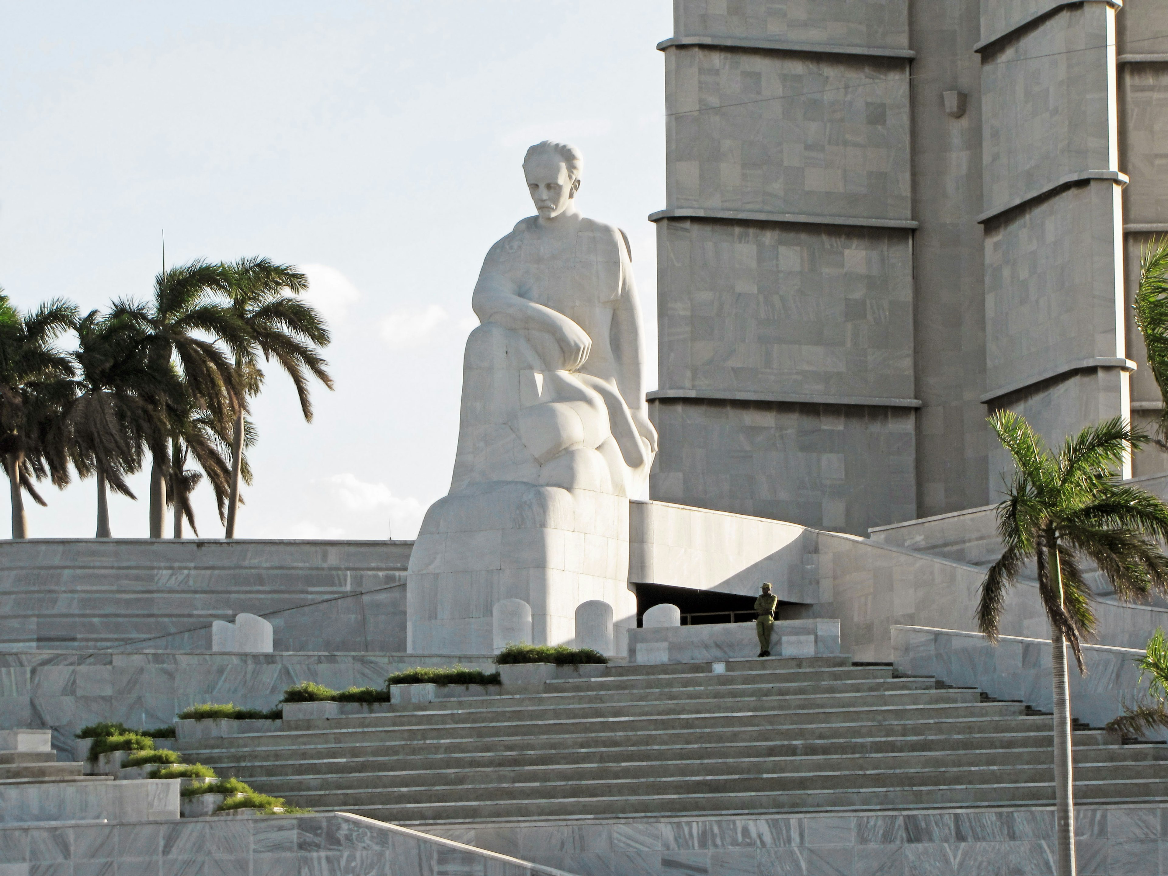 A prominent white statue in a plaza surrounded by palm trees