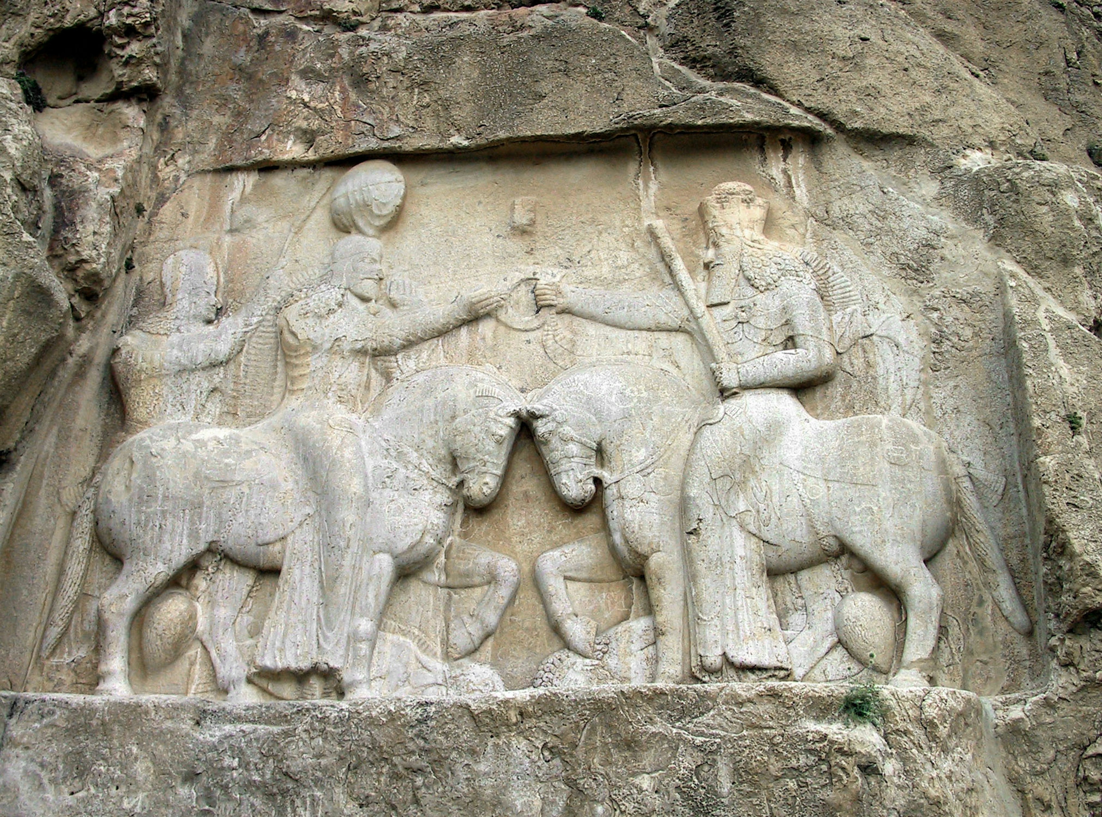 Antigua escultura en roca que representa a dos figuras a caballo interactuando entre sí