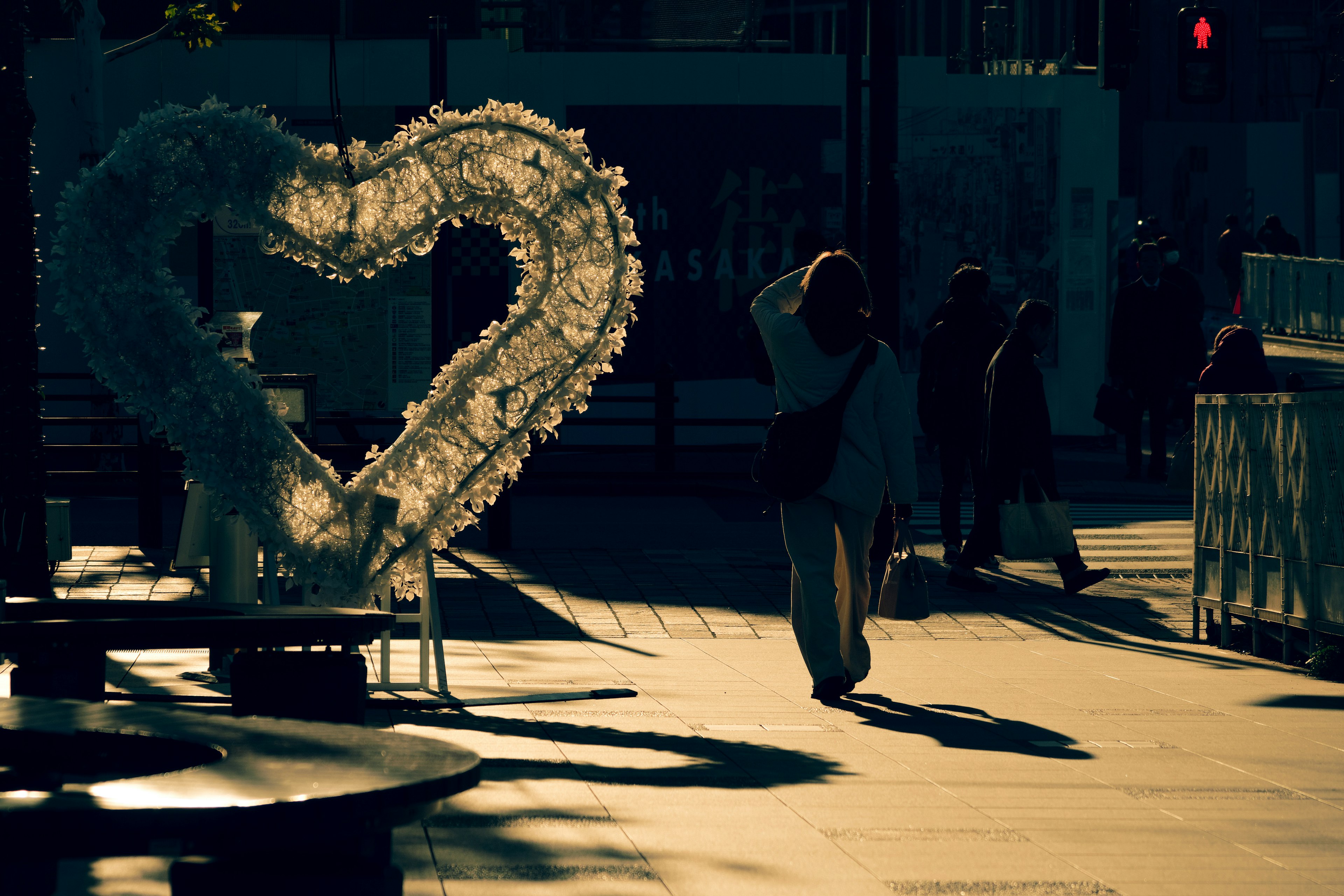 Una escena urbana al anochecer con una gran decoración en forma de corazón y las sombras de las personas