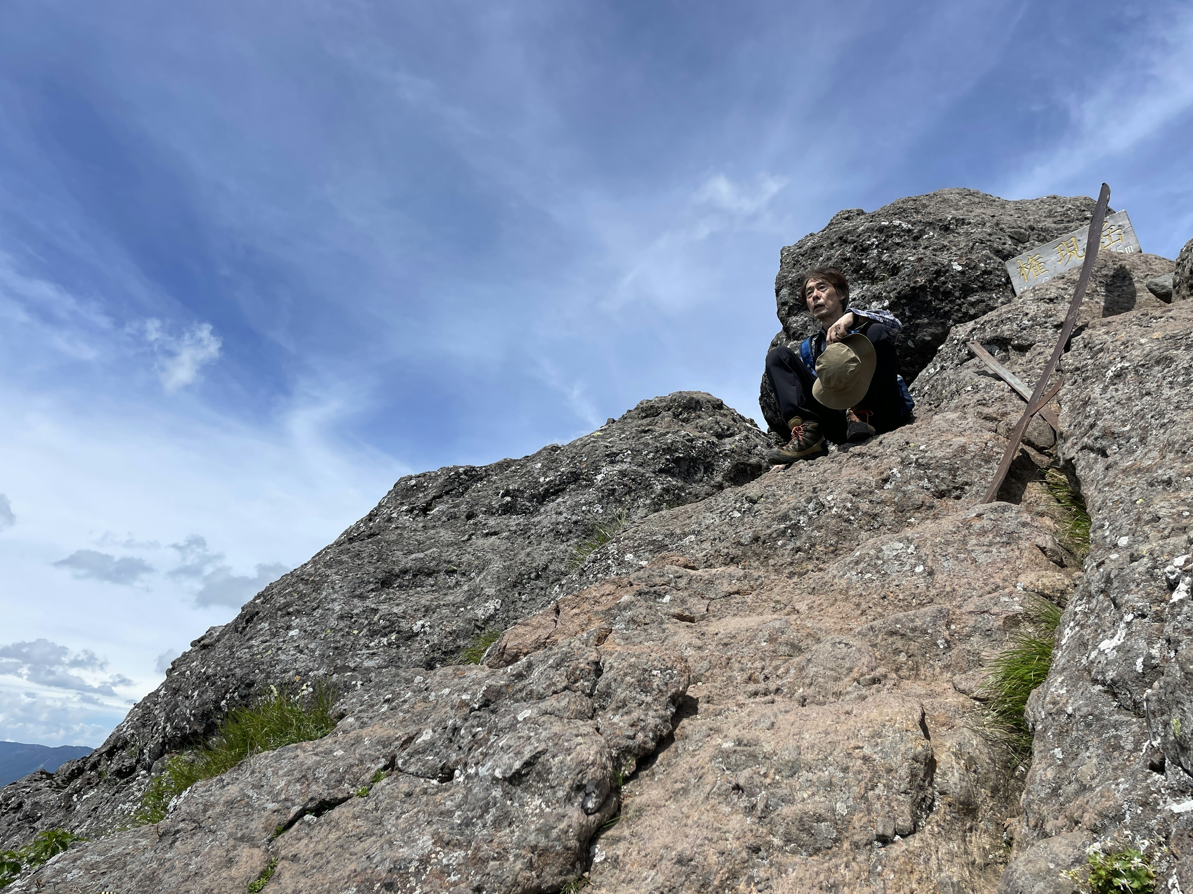 Person sitzt auf einem felsigen Berg mit blauem Himmel im Hintergrund