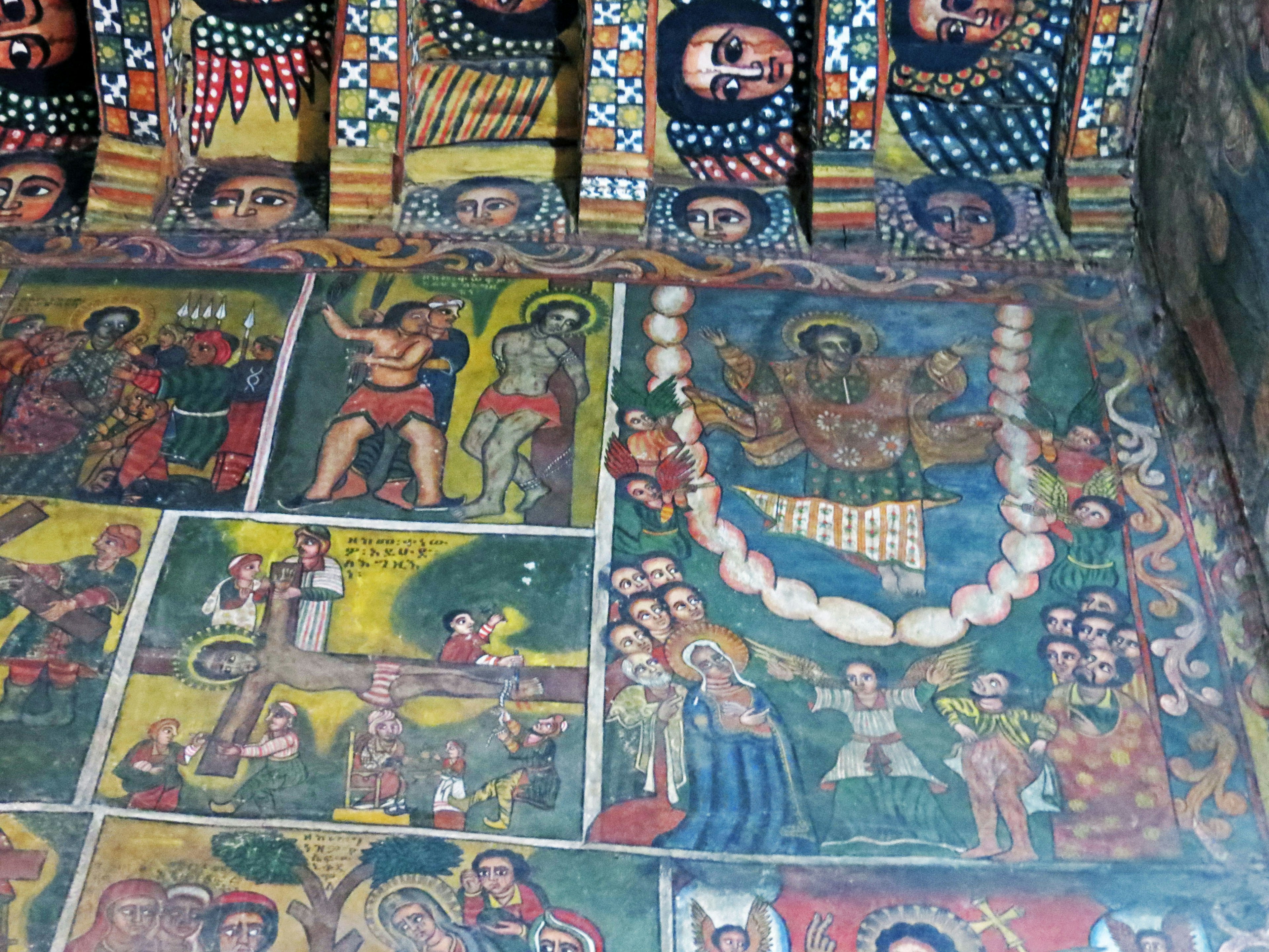 Interior de una iglesia histórica con murales religiosos coloridos en el techo y las paredes