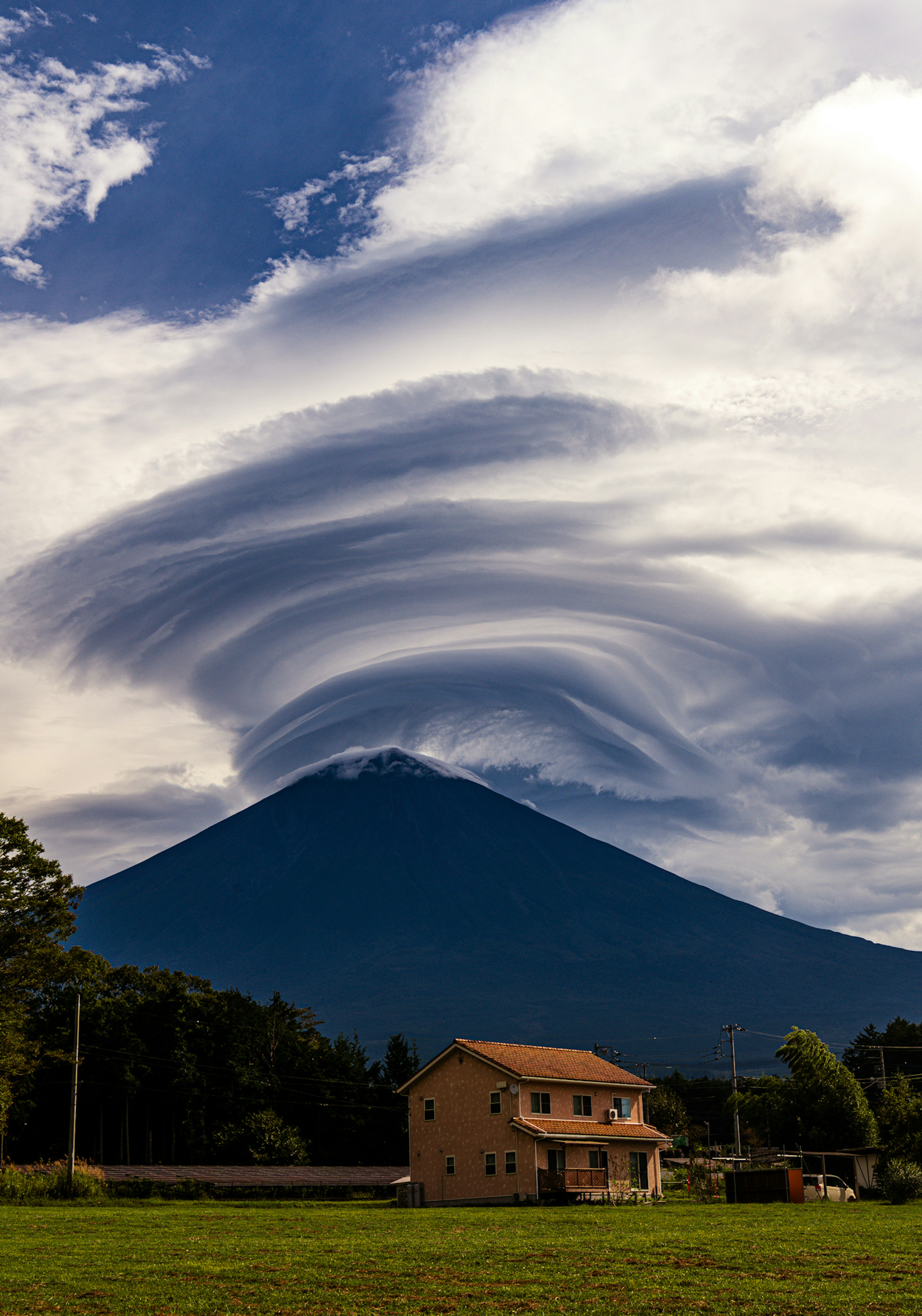 Malersiche Aussicht auf den Fuji mit wirbelnden Wolken und einem nahegelegenen Haus