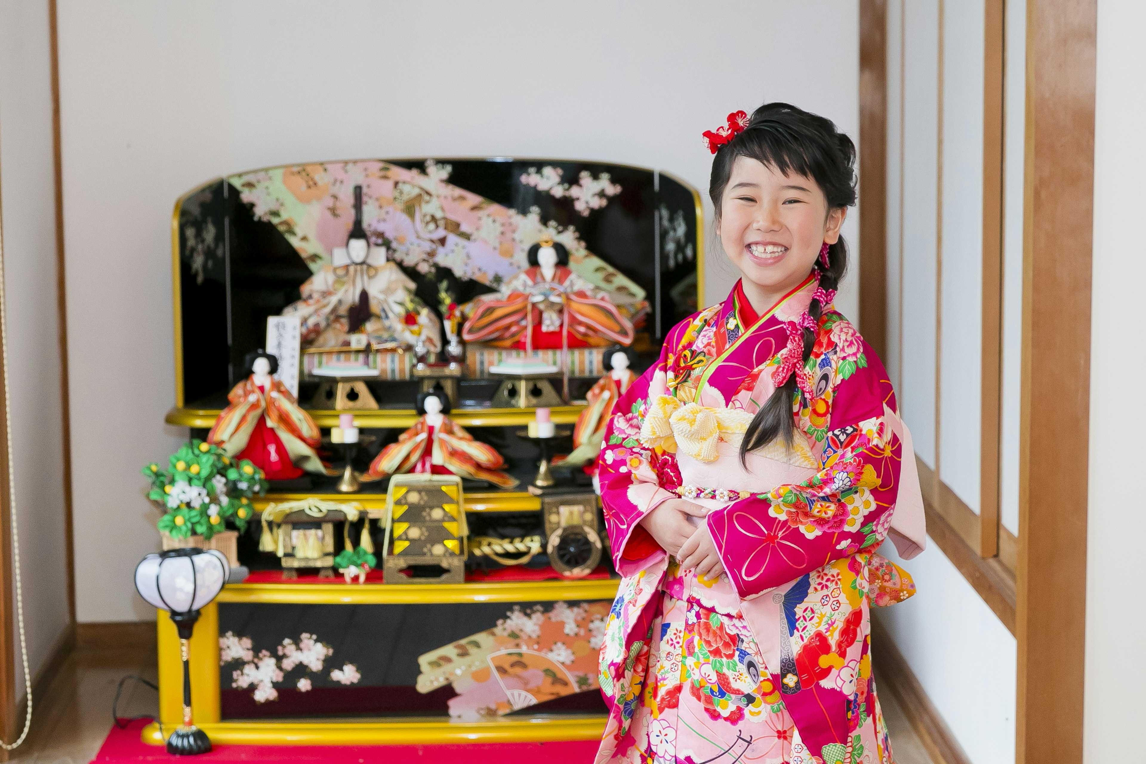 Una niña con un kimono colorido sonriendo con una exhibición tradicional de muñecas hina al fondo