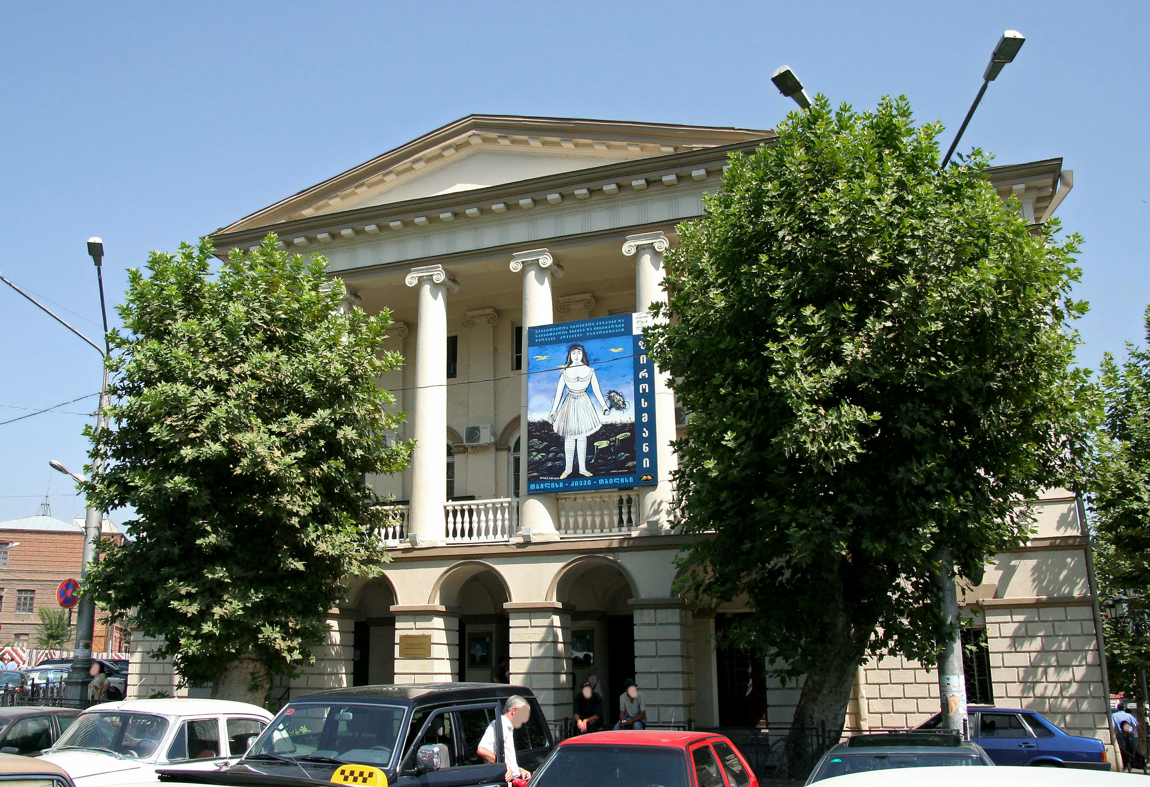 Edificio storico con un grande poster blu e alberi verdi davanti