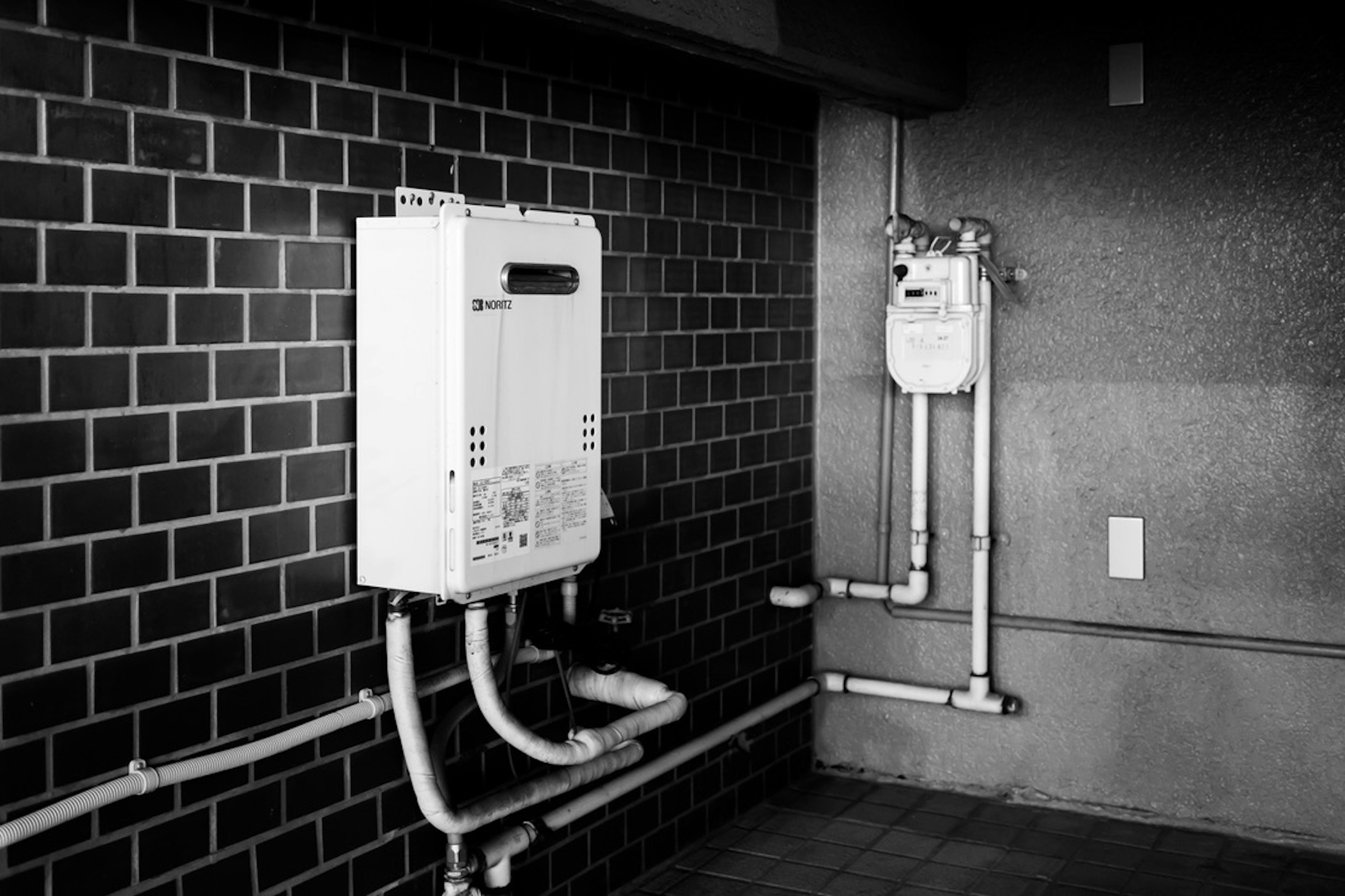 Imagen de un calentador de agua y un medidor de gas montados en una pared de azulejos negros