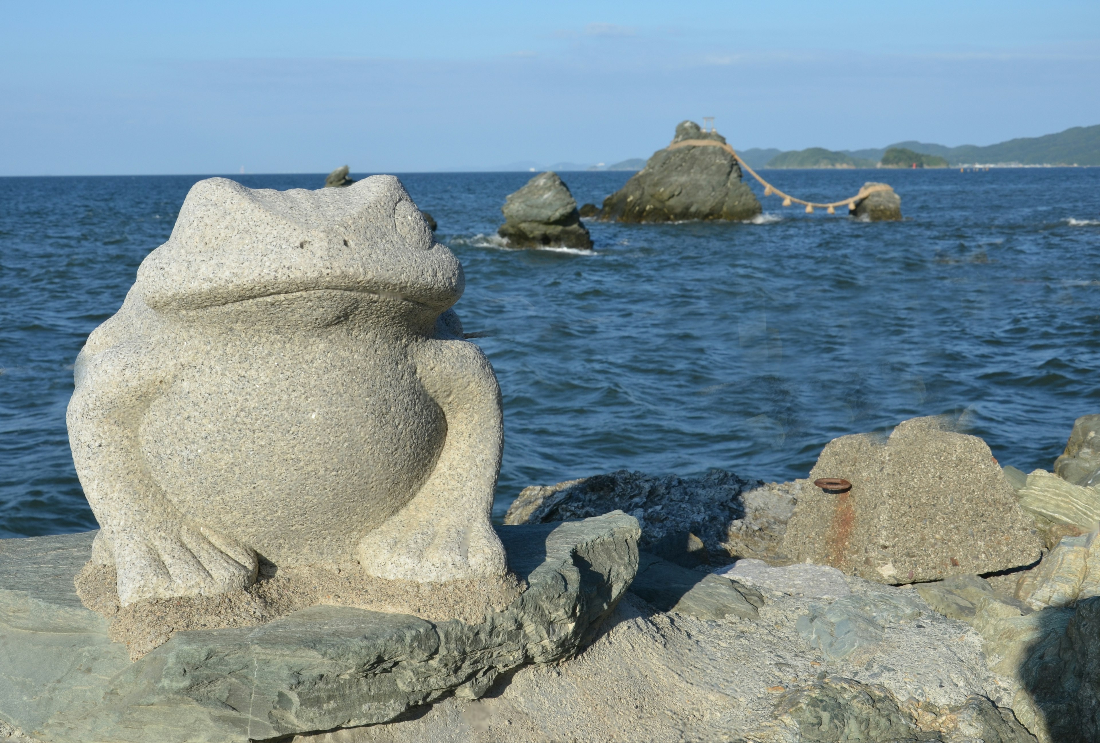 Eine Steinfroschskulptur nahe dem Wasser mit Felsen im Hintergrund