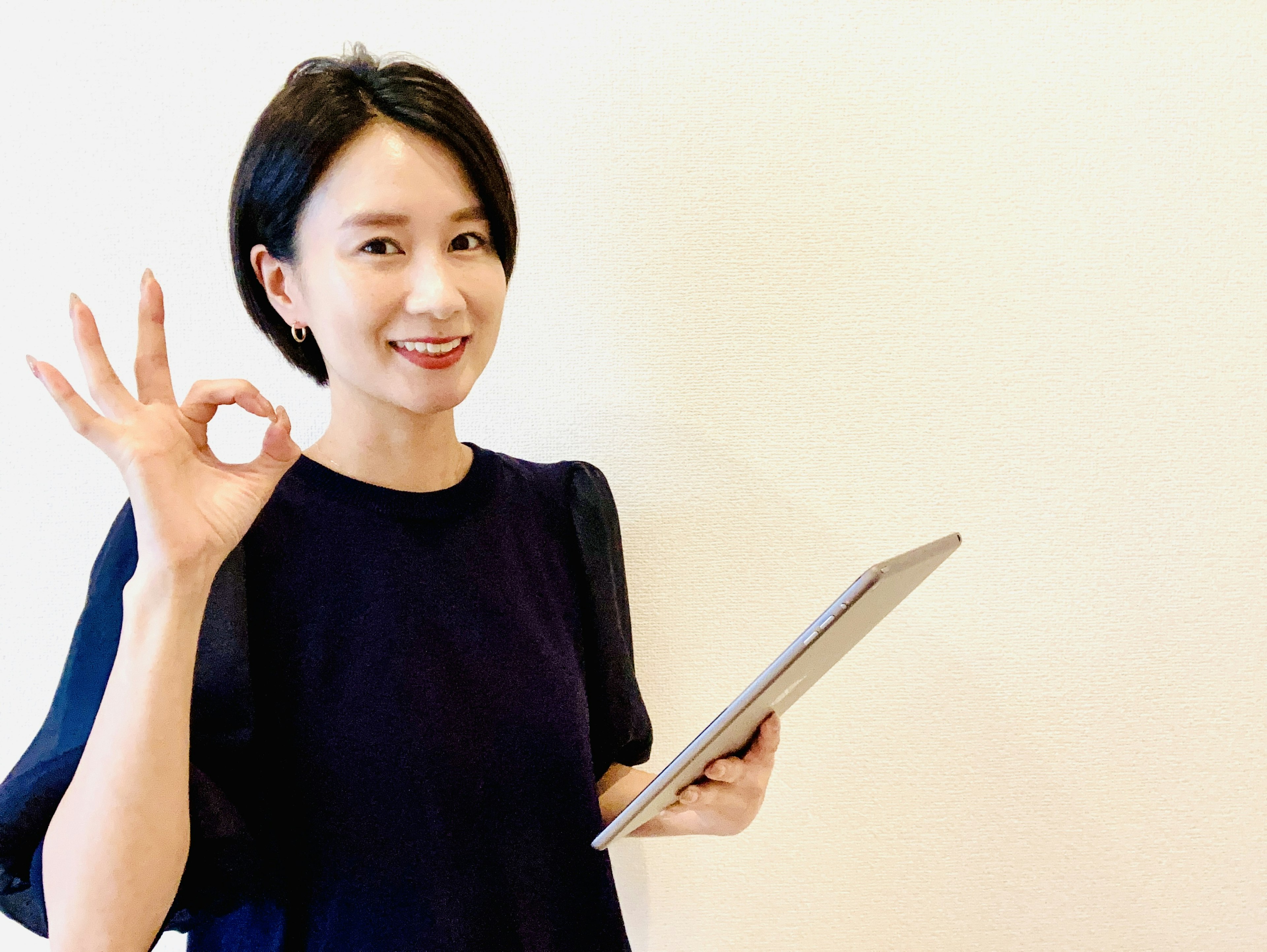 A woman holding a tablet and smiling while showing an OK sign