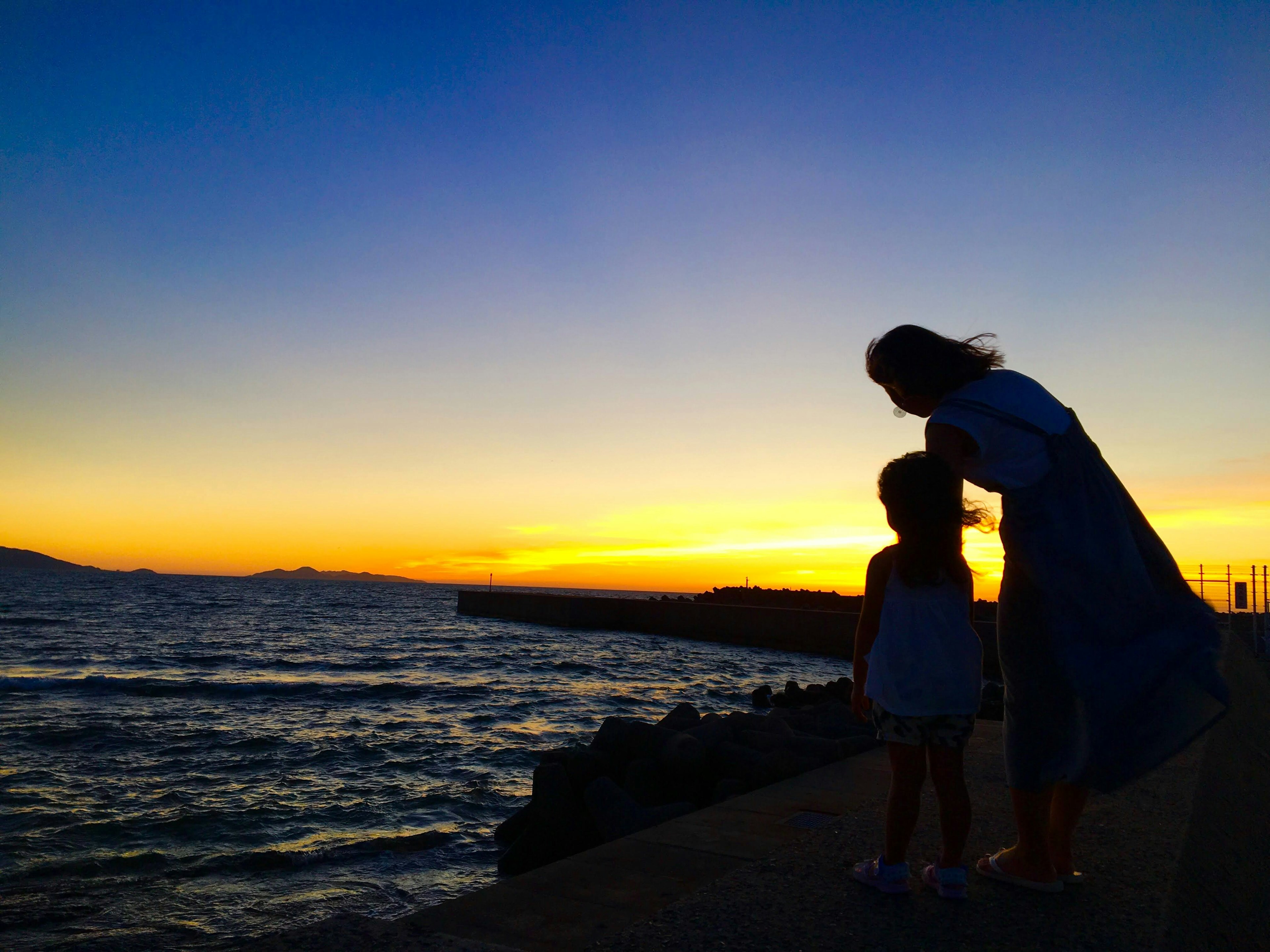 Silhouette einer Mutter und Tochter vor einem Sonnenuntergang am Strand