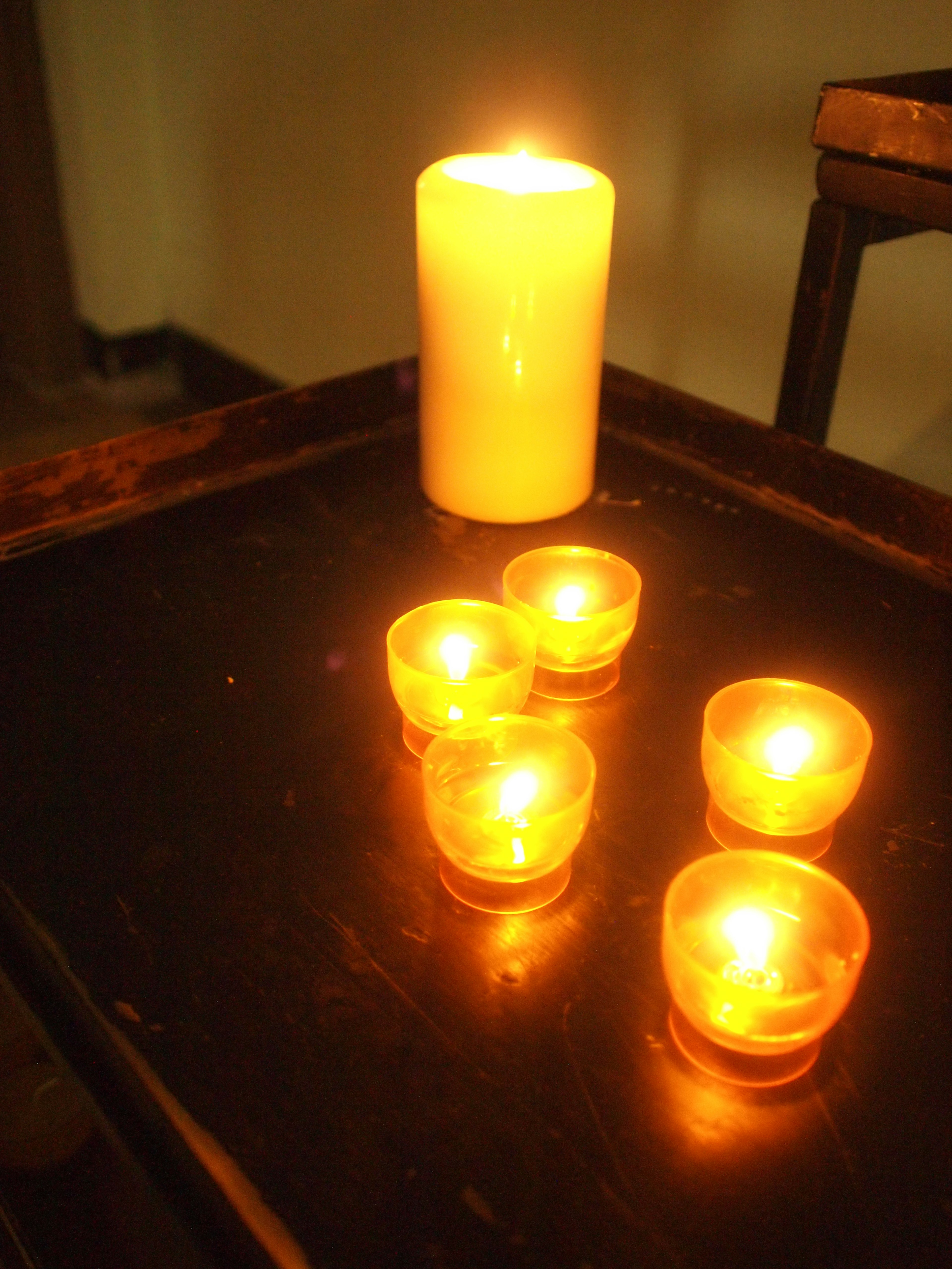 Una escena de luz de vela cálida con una vela blanca alta y cuatro velas votivas más pequeñas sobre una mesa oscura