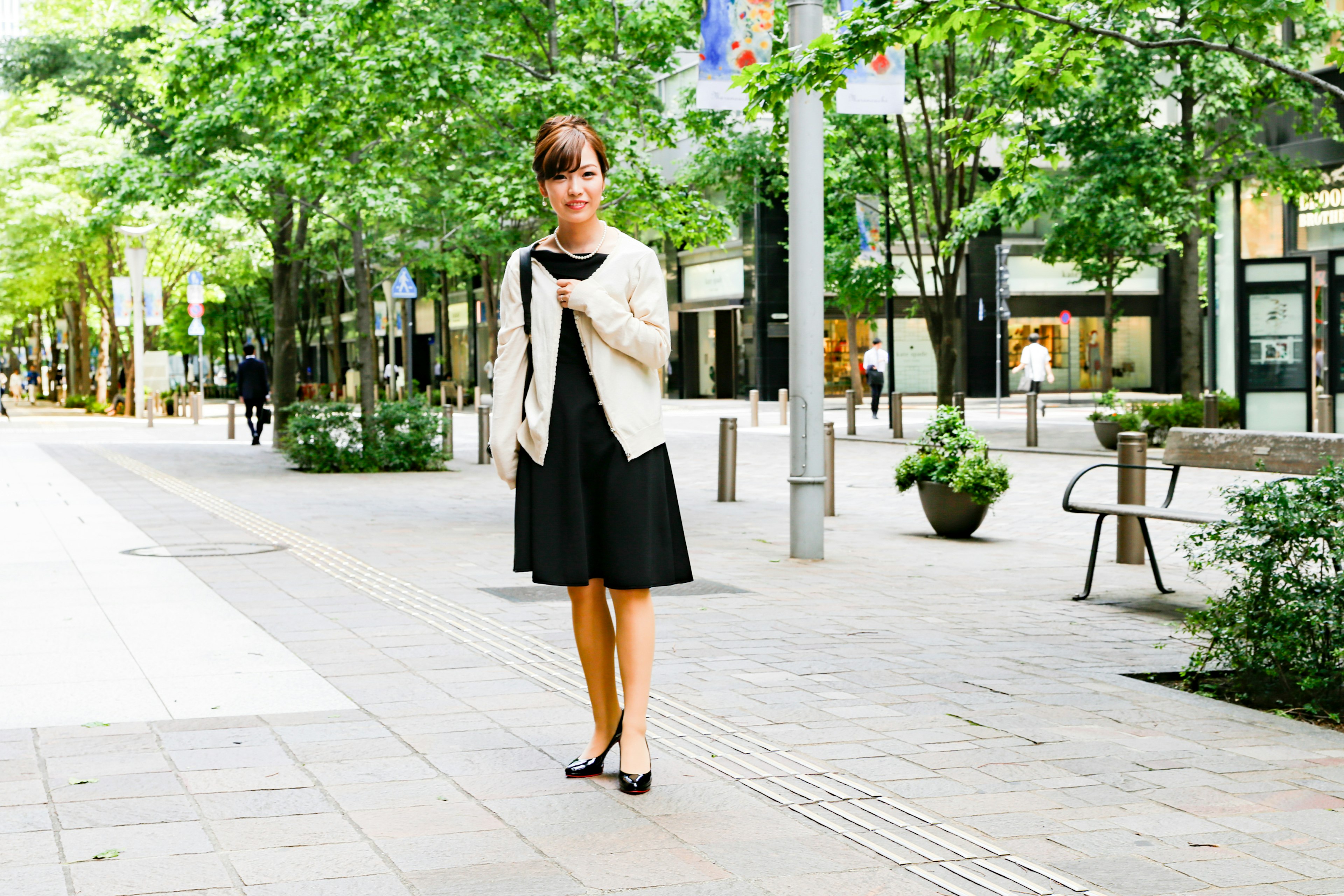 A woman in a black dress and white jacket standing in a park