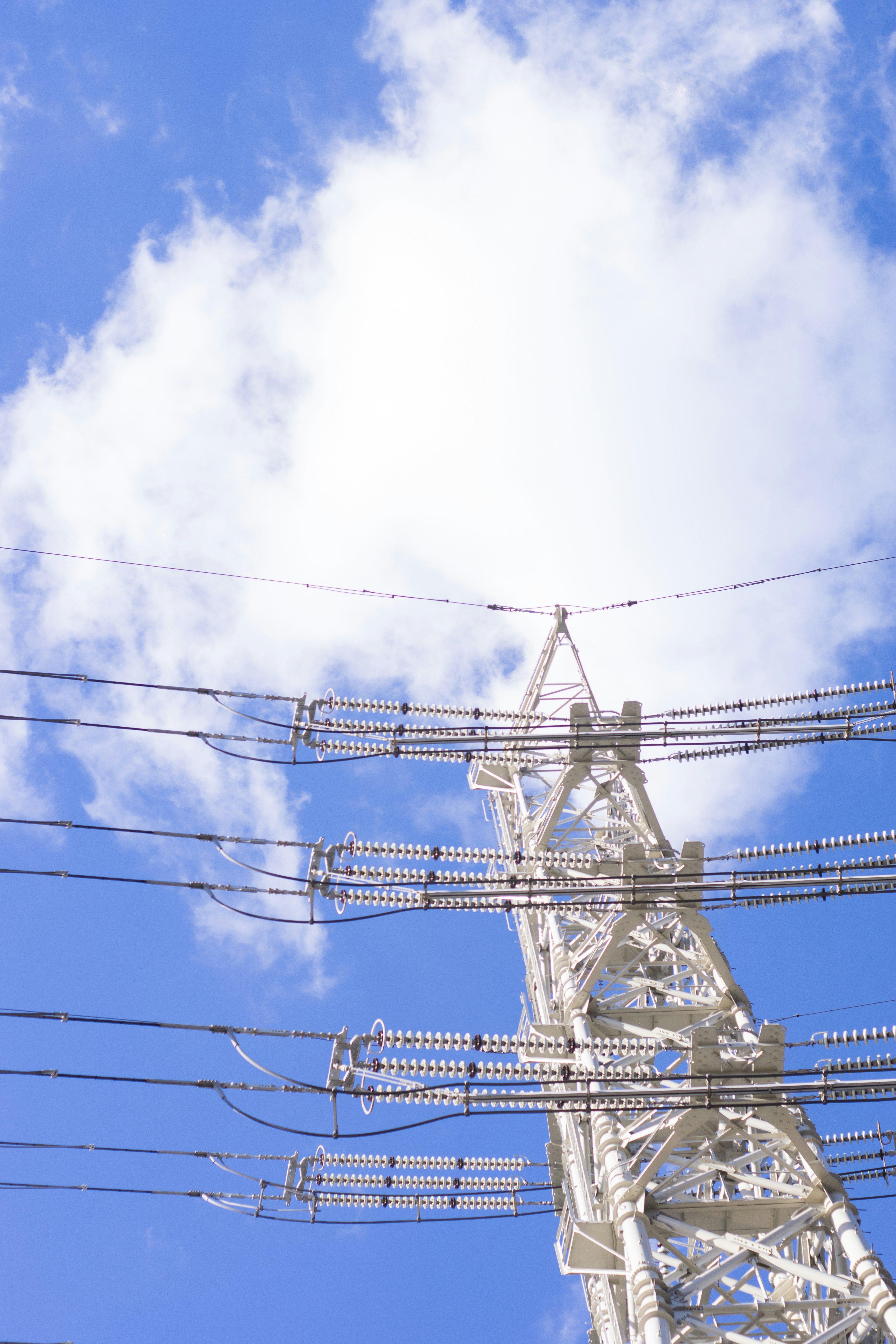 Weißer Strommast vor einem blauen Himmel mit flauschigen Wolken