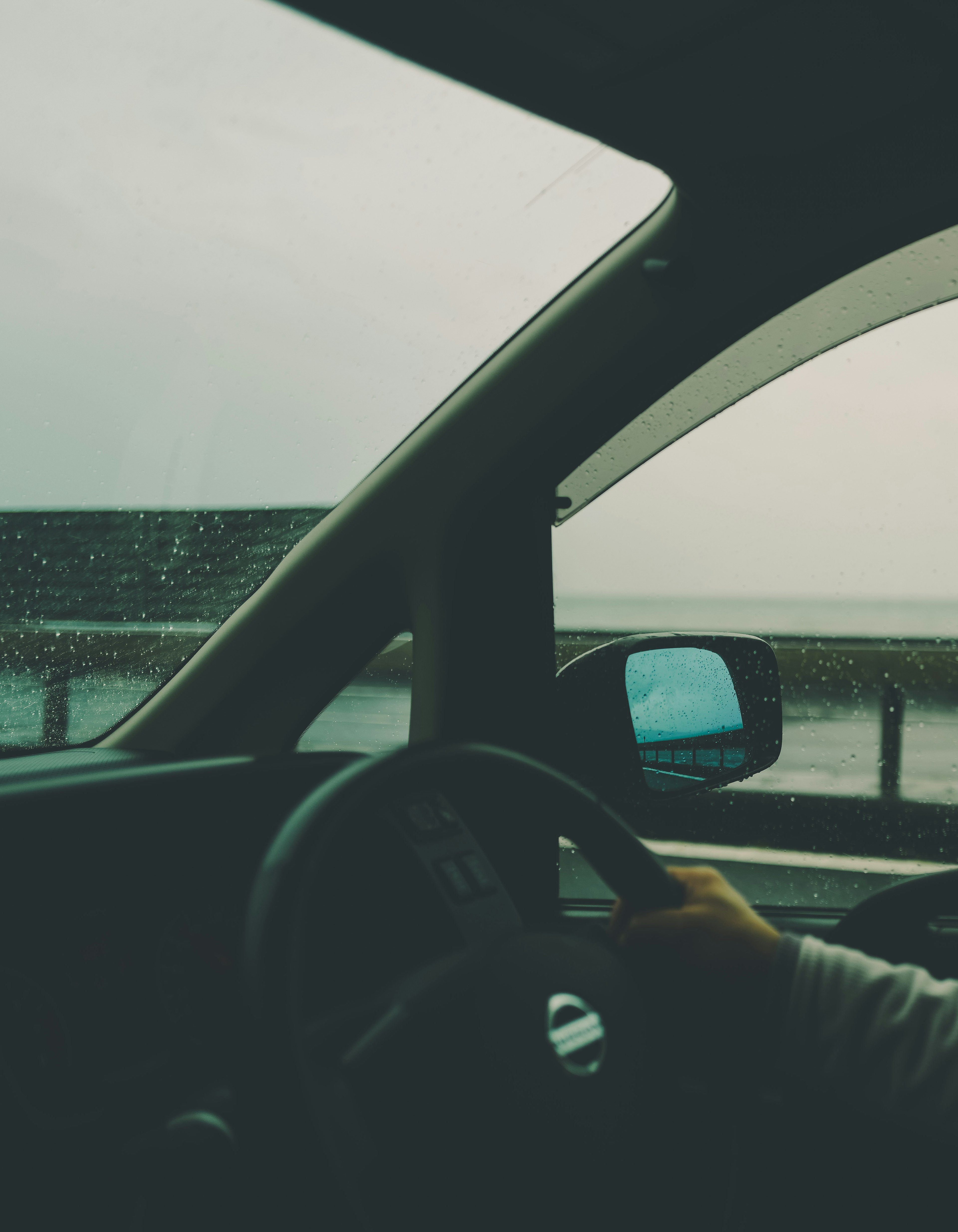 Hand on steering wheel inside a car during rain with ocean view