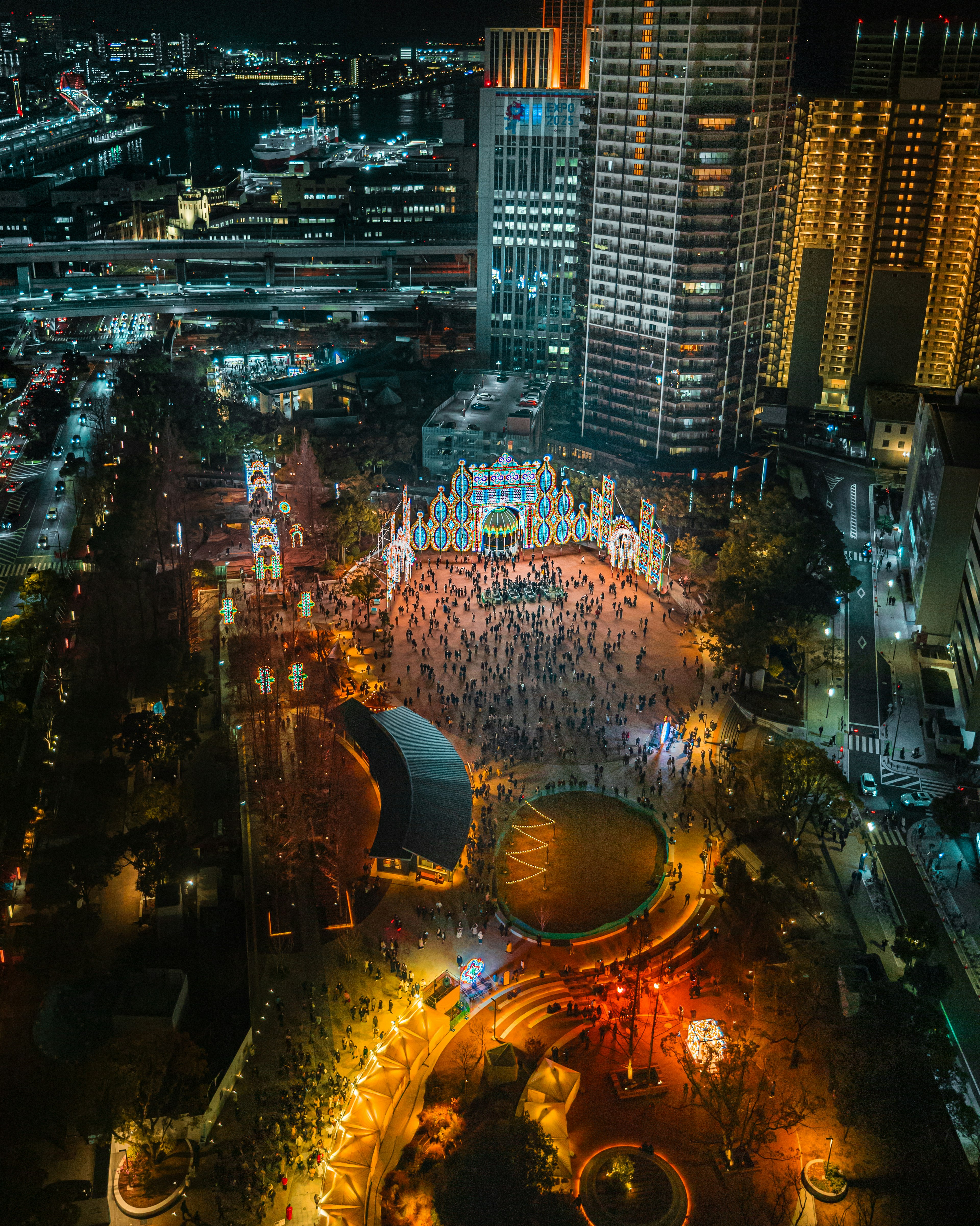 Vista aérea de una ciudad vibrante de noche con luces brillantes y una plaza concurrida