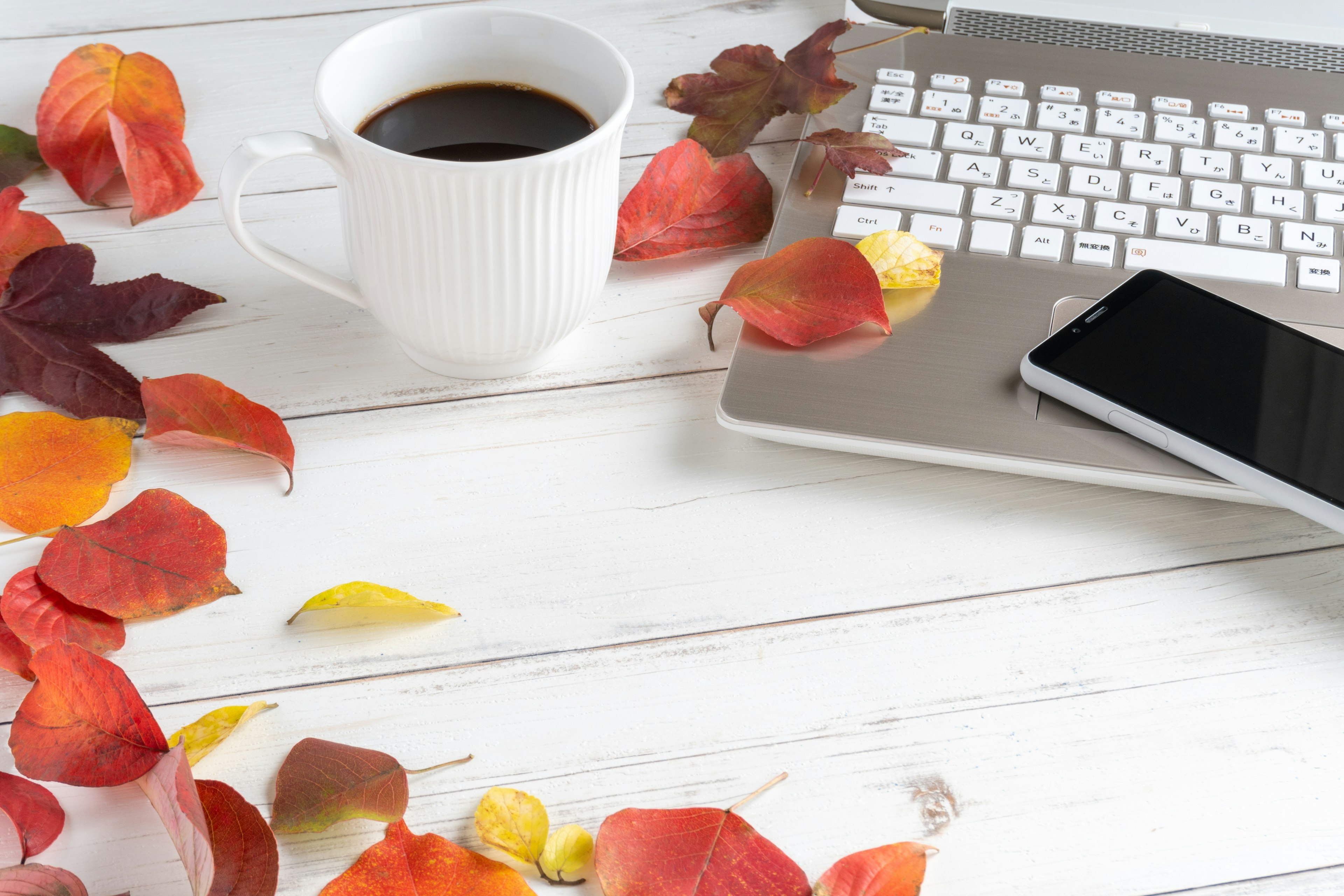 Coffee cup laptop smartphone scattered autumn leaves on desk