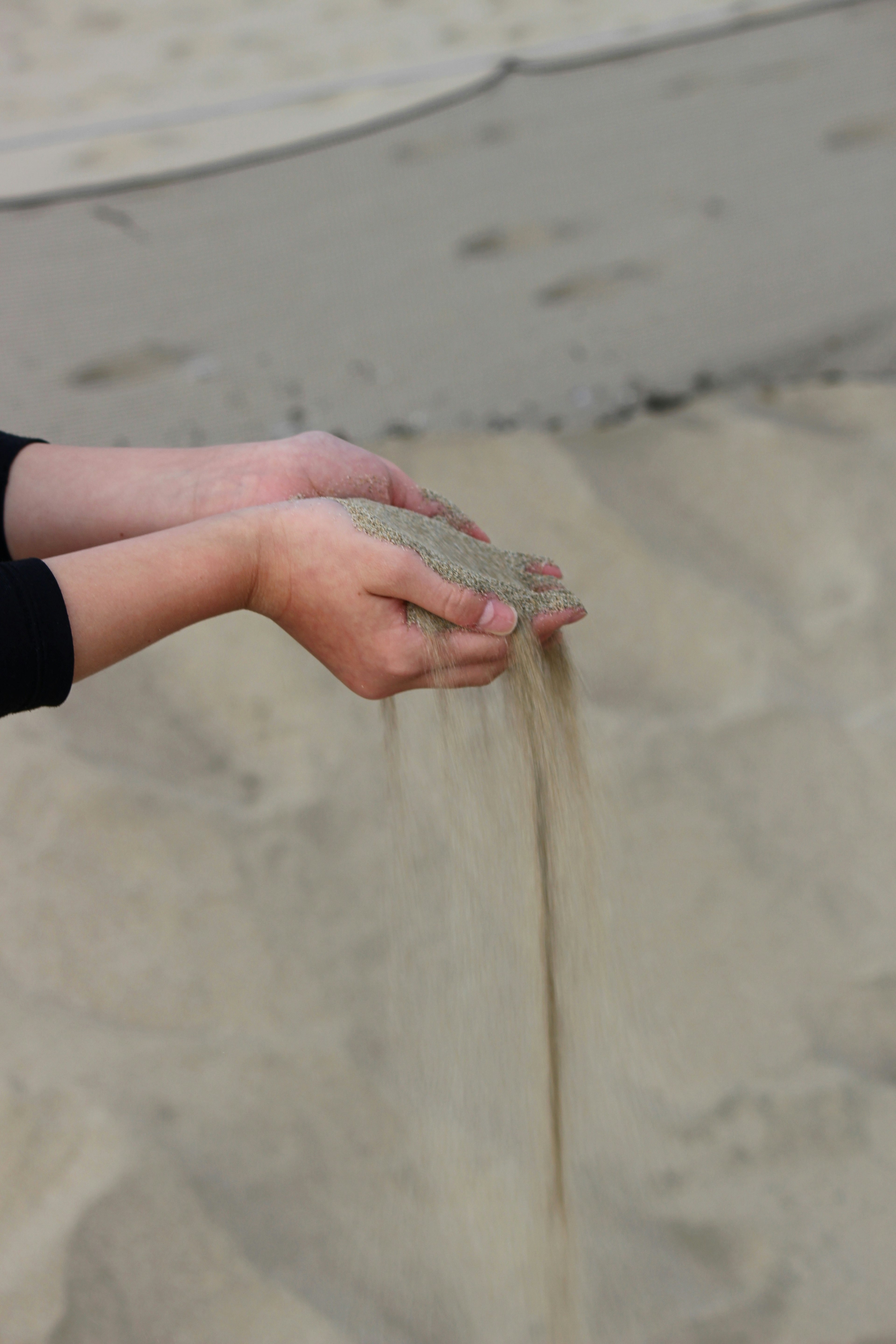 Mani che rilasciano sabbia su una spiaggia