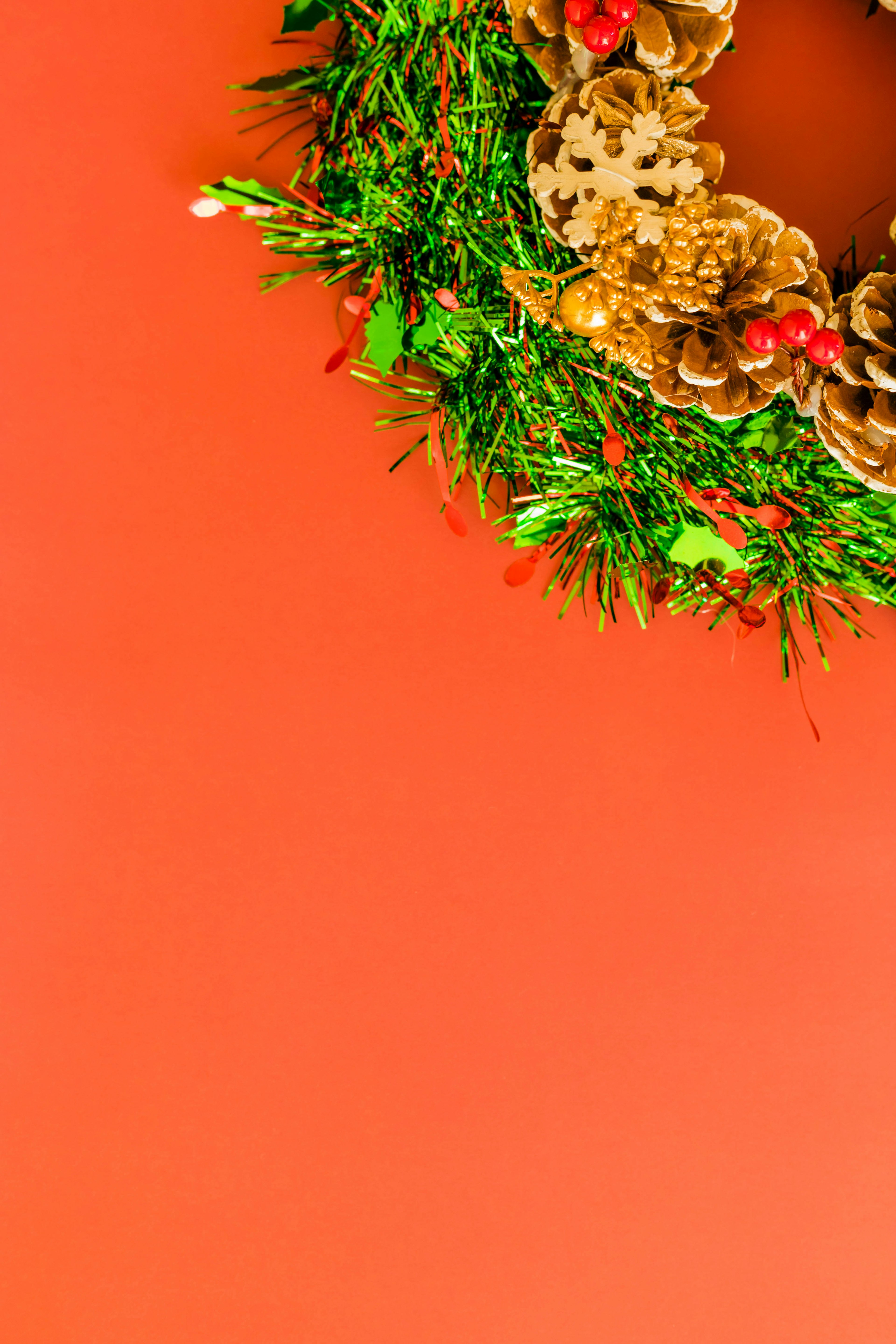 Corona de Navidad decorada con piñas y hojas verdes sobre un fondo naranja