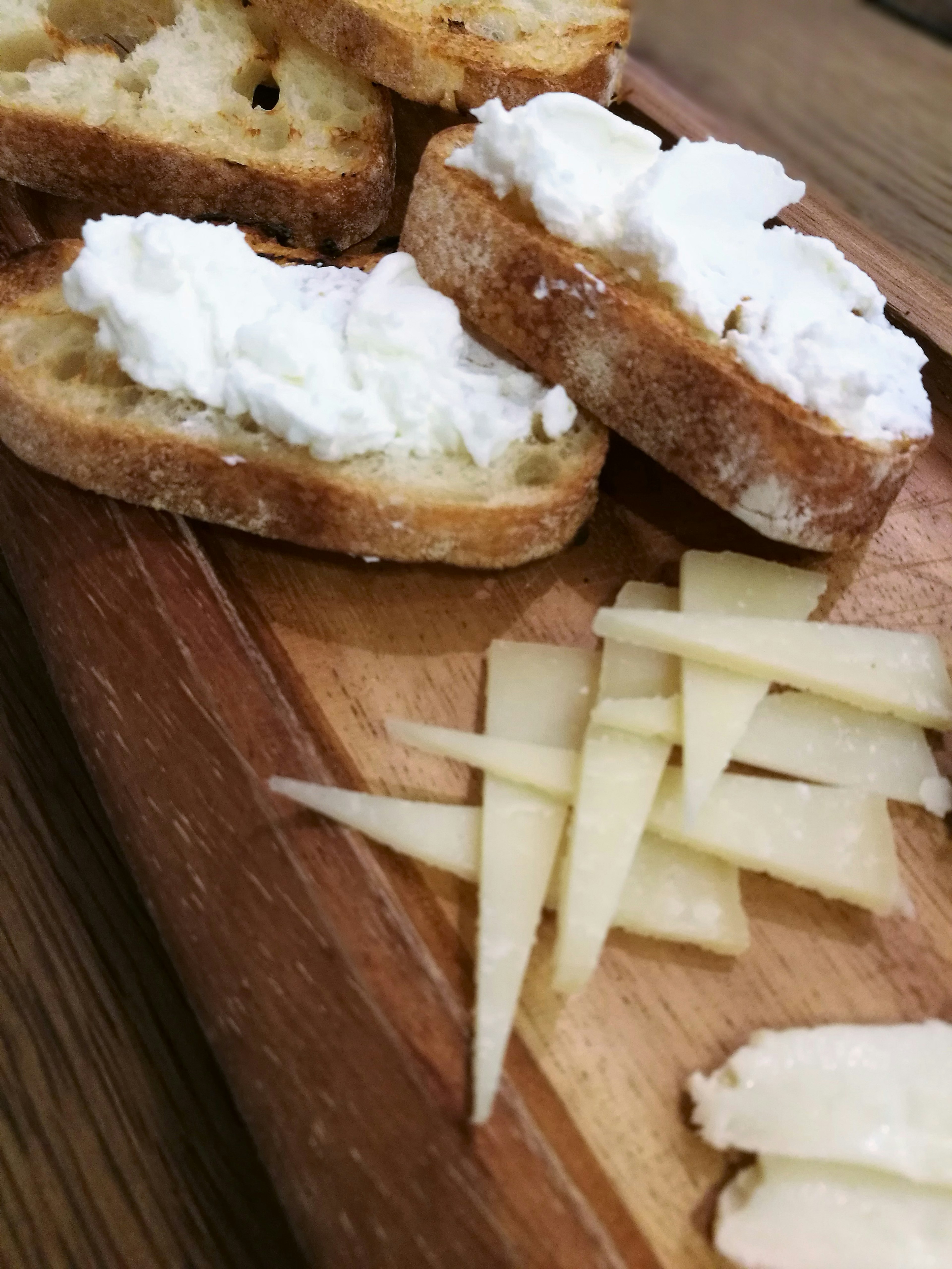 Geröstetes Brot mit Frischkäse und Käsescheiben auf einem Holzbrett