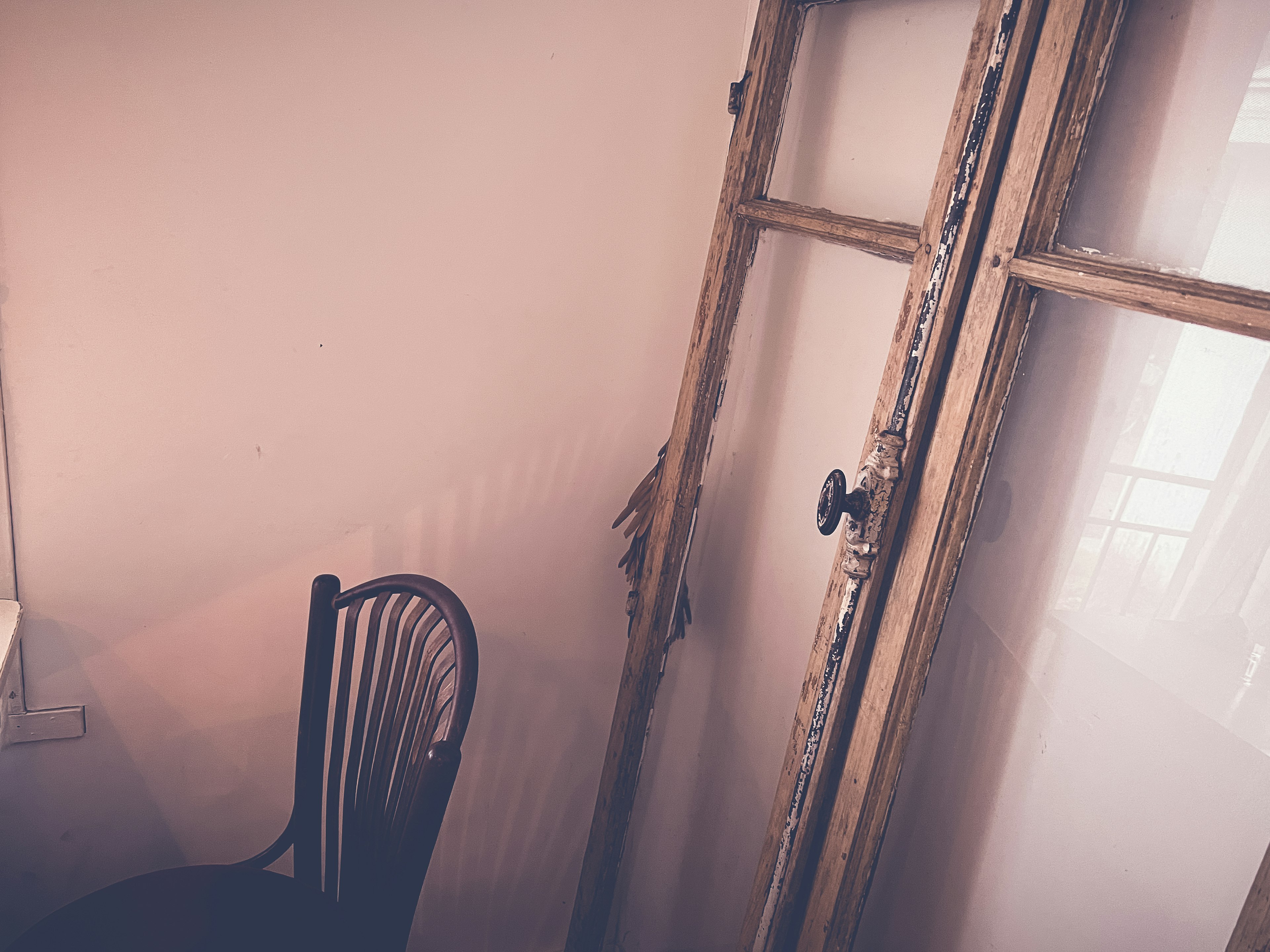 A corner of a simple room featuring a wooden chair and an old wooden window frame