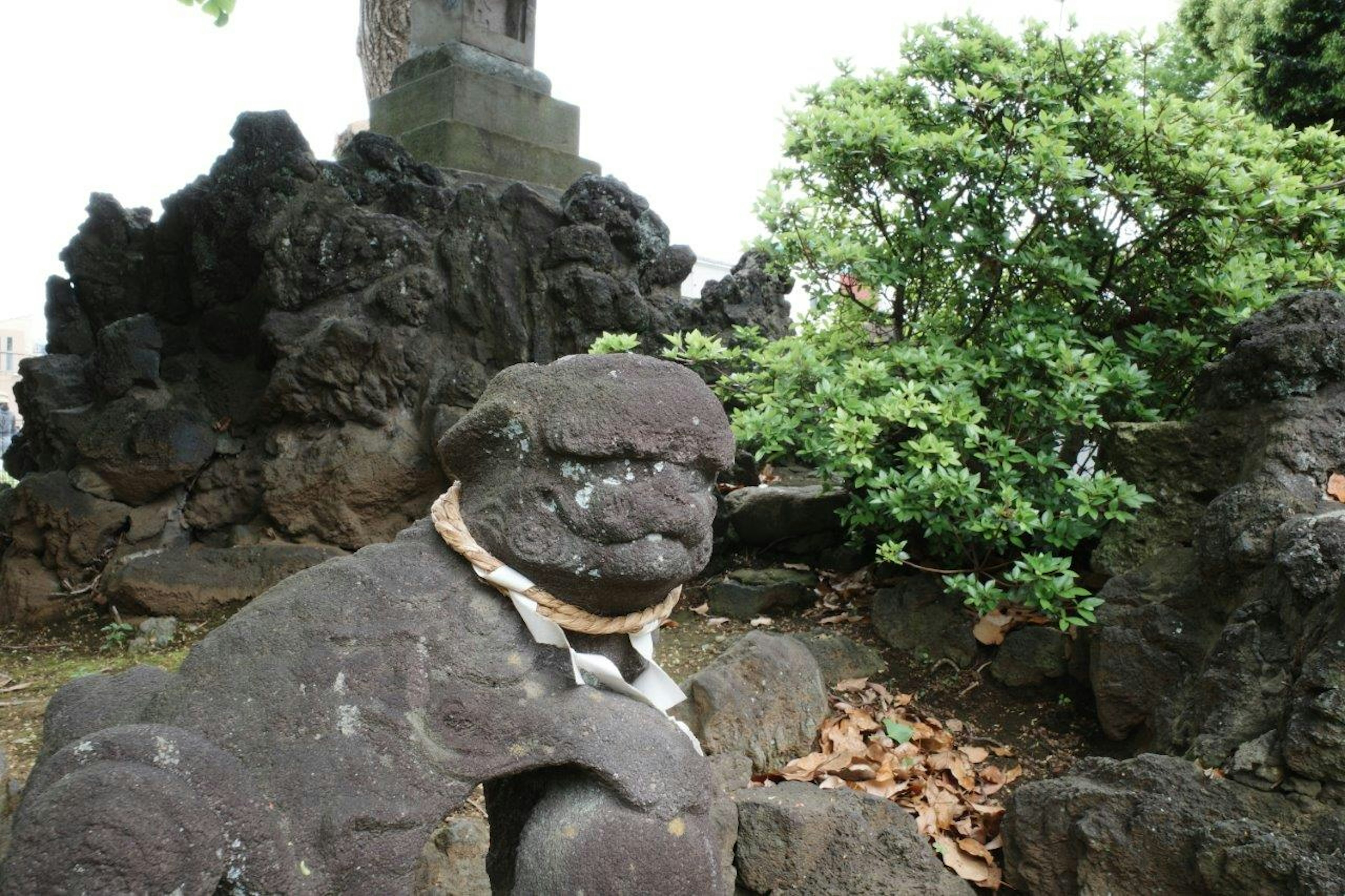 Escultura de león de piedra sentada entre rocas y vegetación