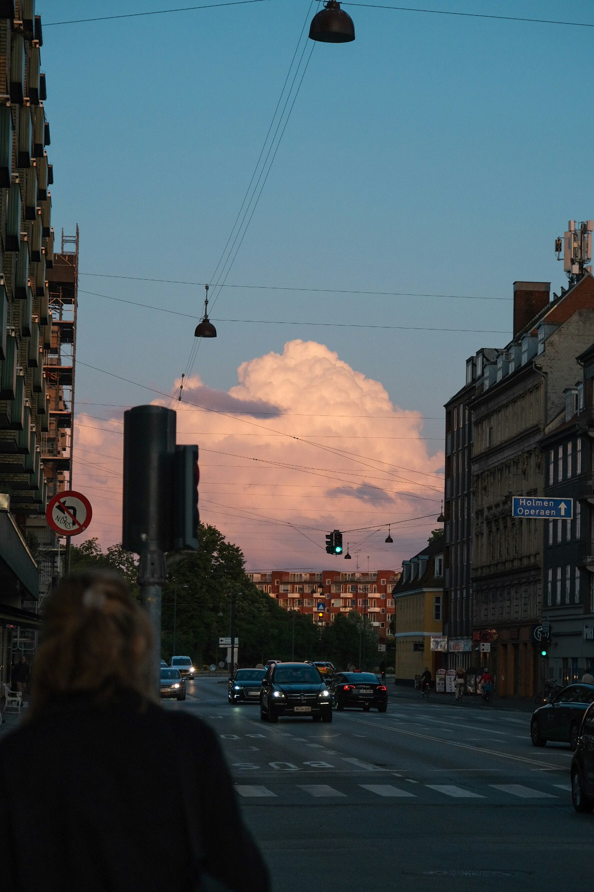 A person standing on a street at dusk with a beautiful cloud in the background