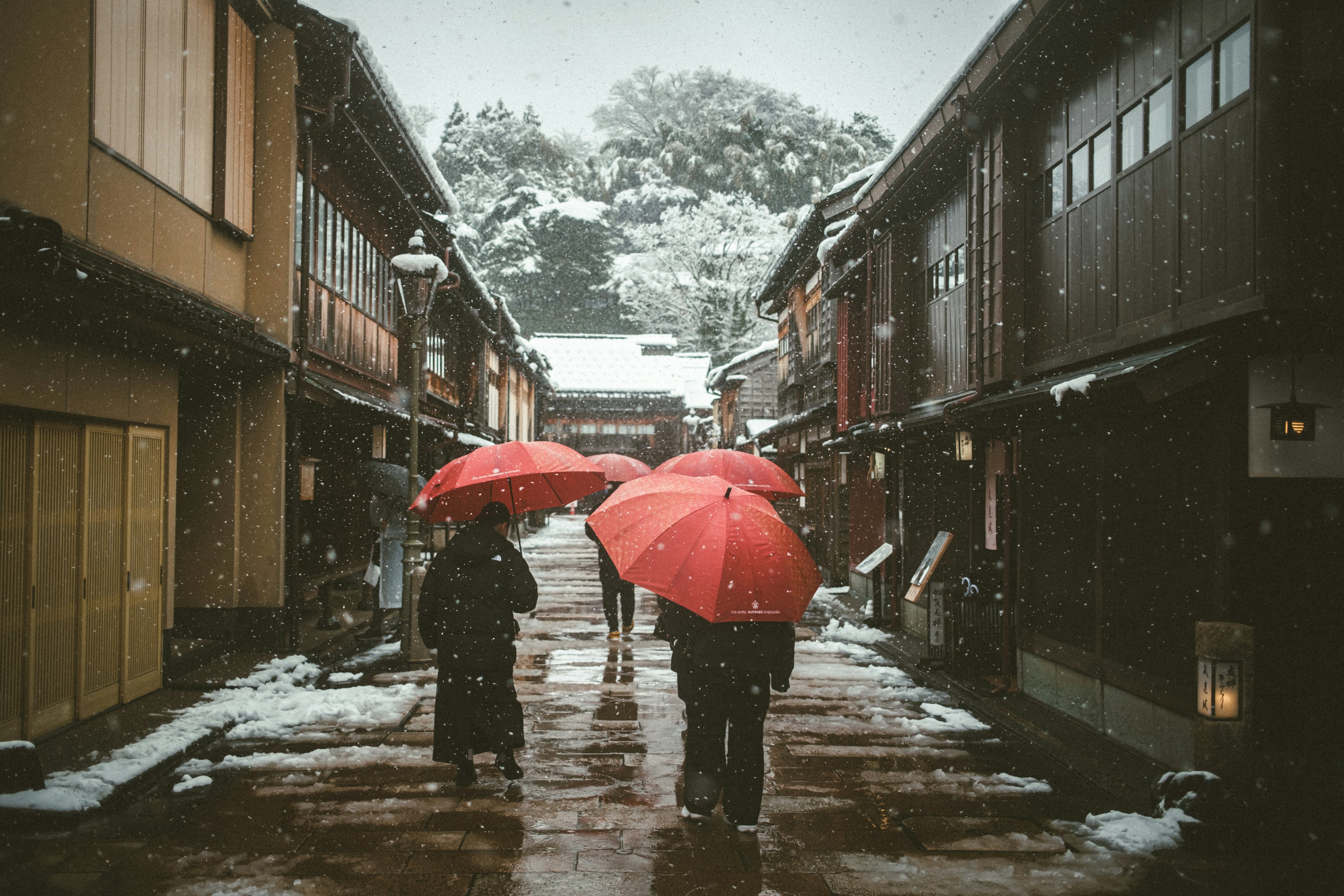 Des gens marchant sous des parapluies rouges dans une rue historique enneigée