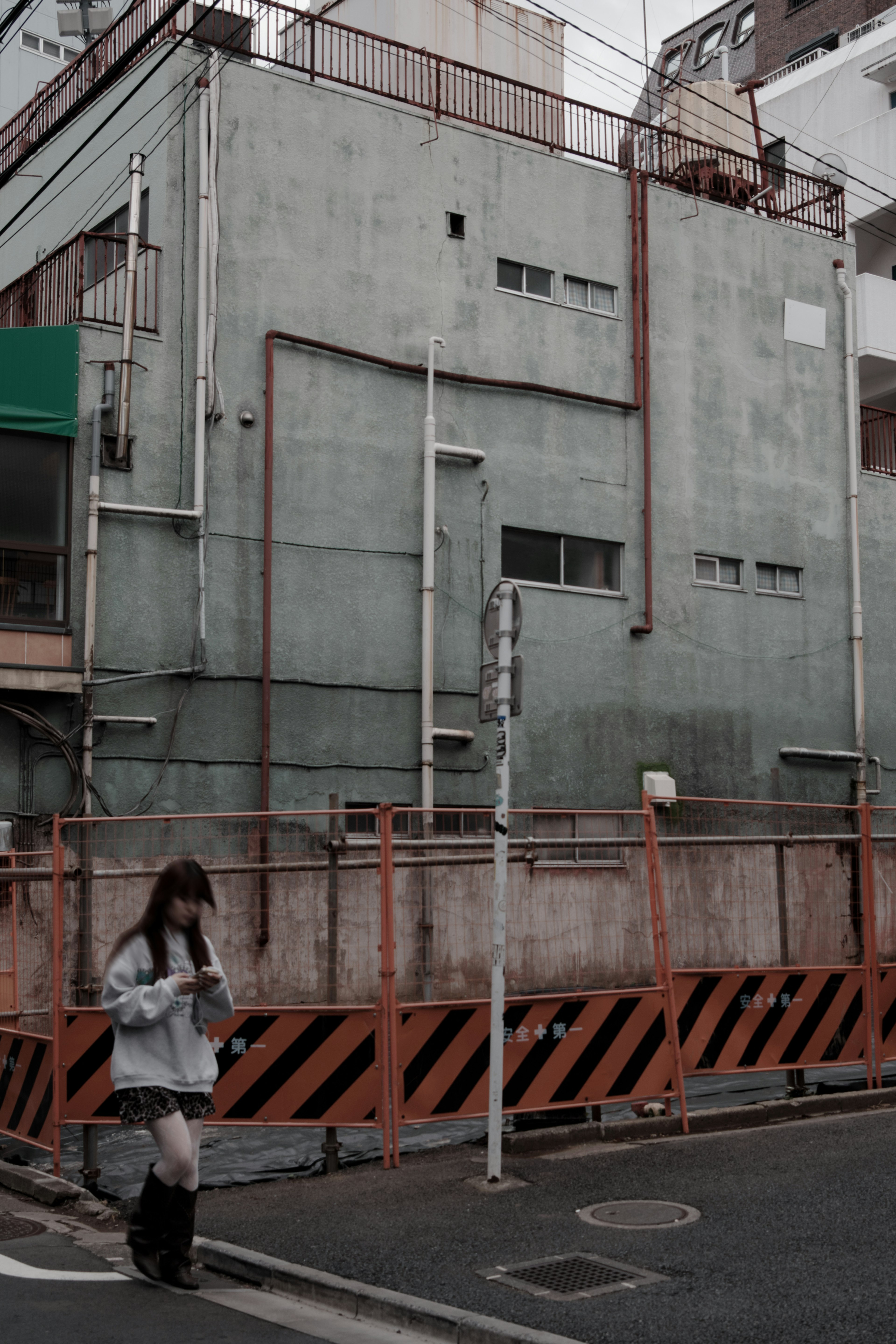 A woman standing at a street corner with a green wall building and construction fence