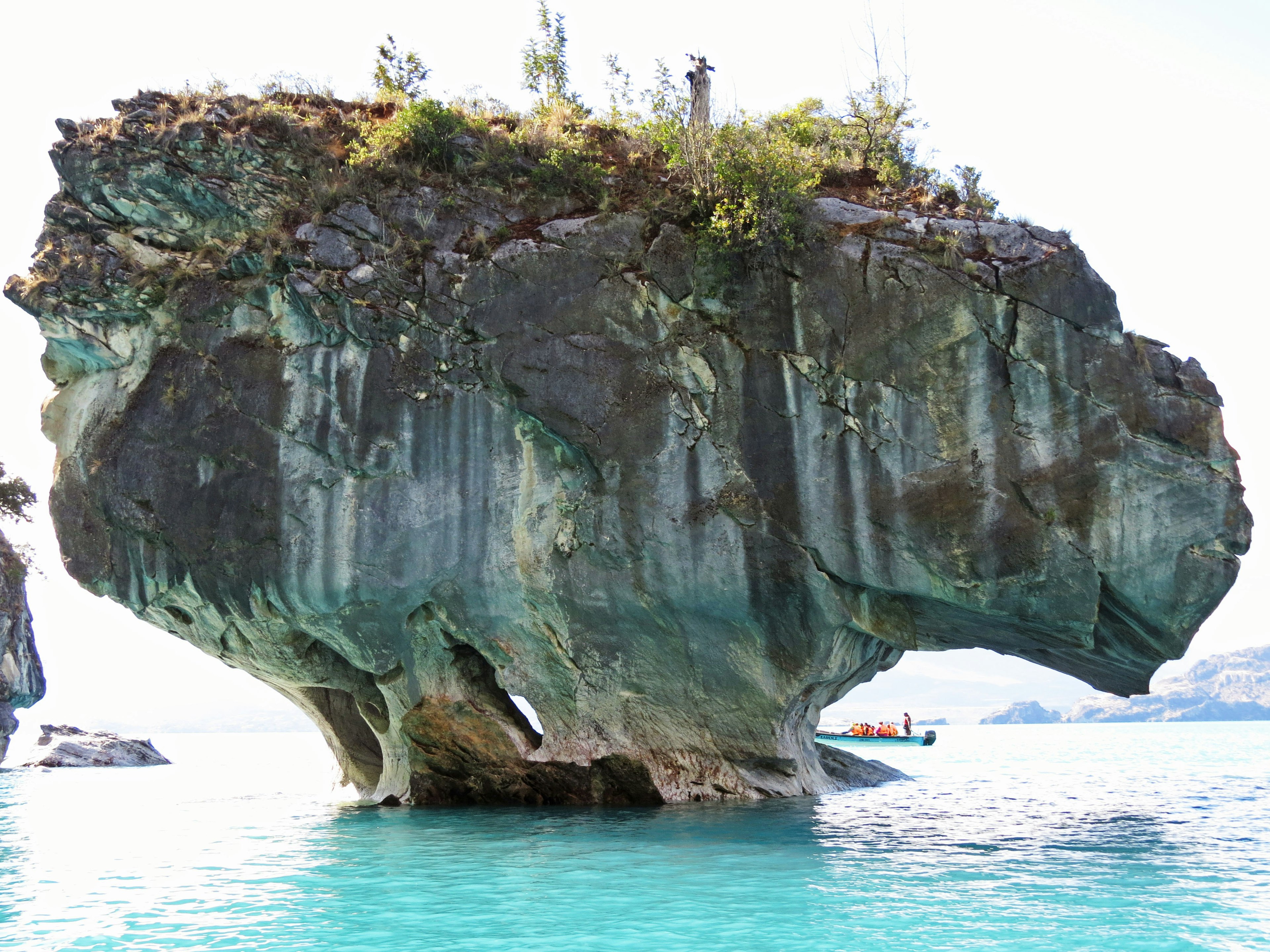 Large rock formation surrounded by turquoise water with greenery on top