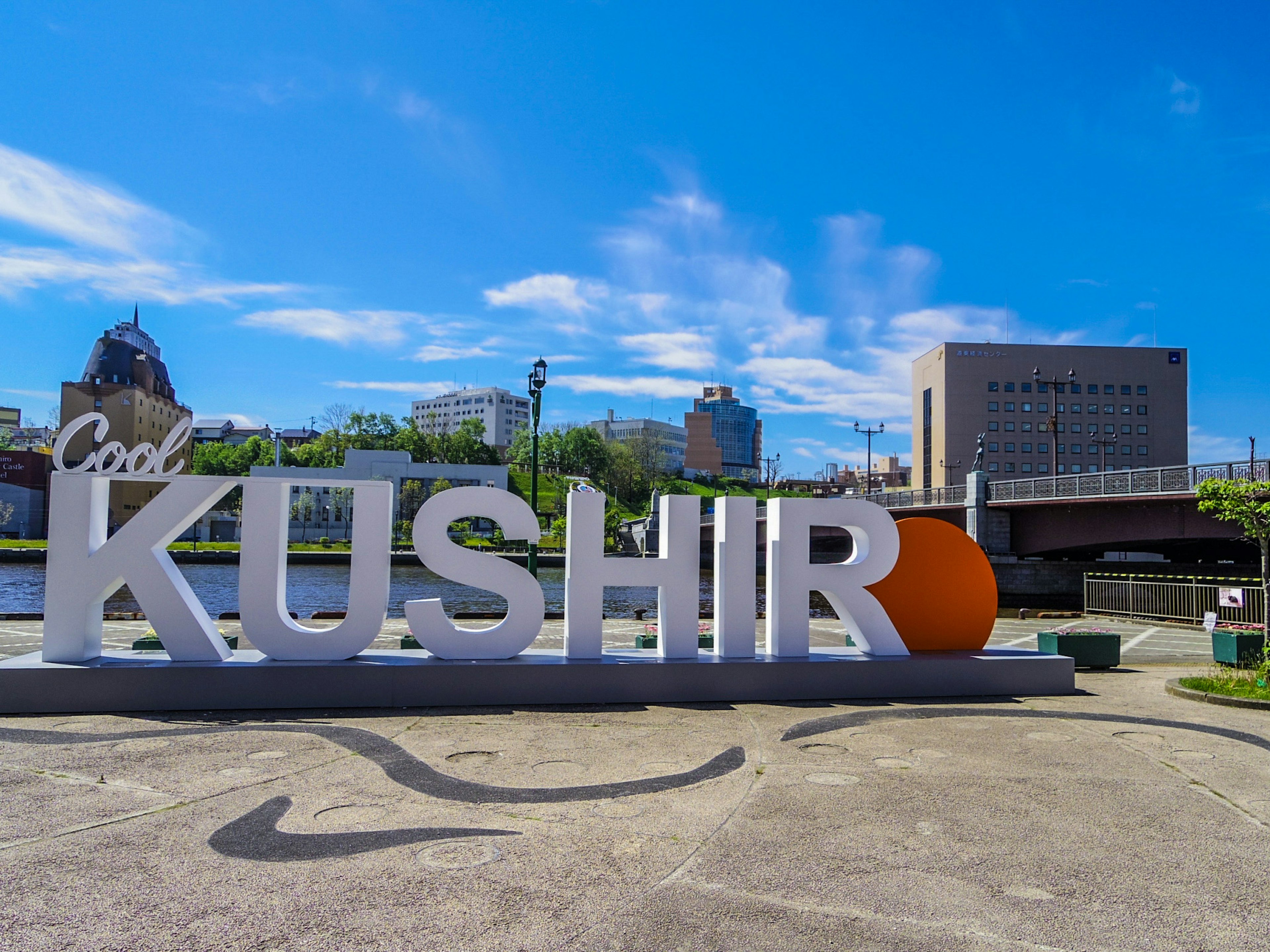 Papan besar bertuliskan KUSHIRO dengan lingkaran oranye di bawah langit biru yang cerah