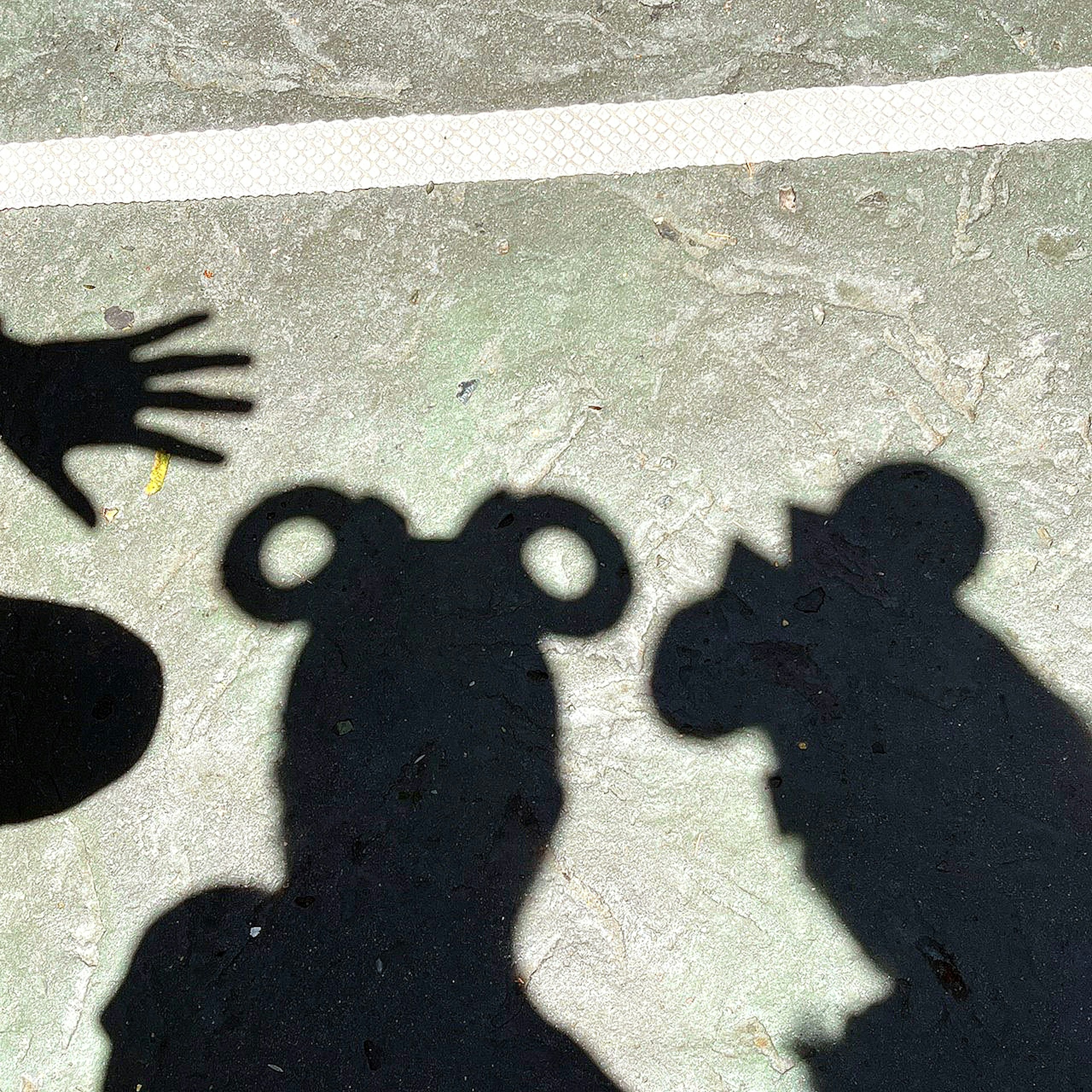 Shadows of a hand and Mickey Mouse ears on concrete ground