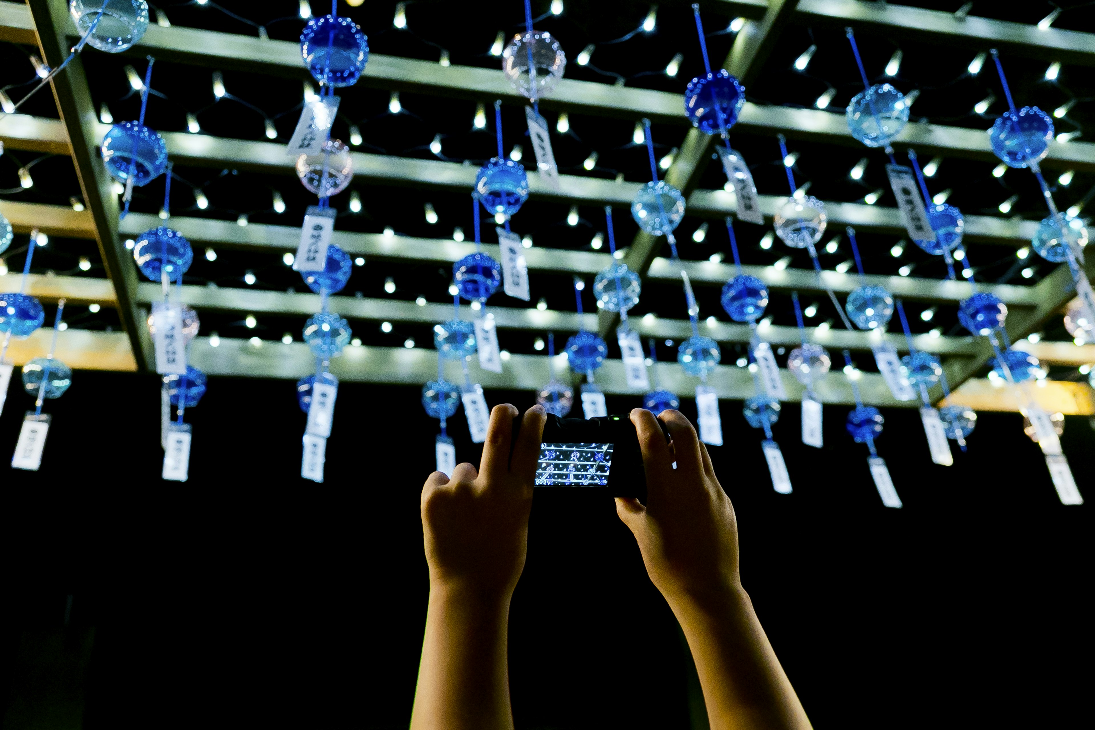 Outdoor display of blue wind chimes hanging with hands holding a smartphone