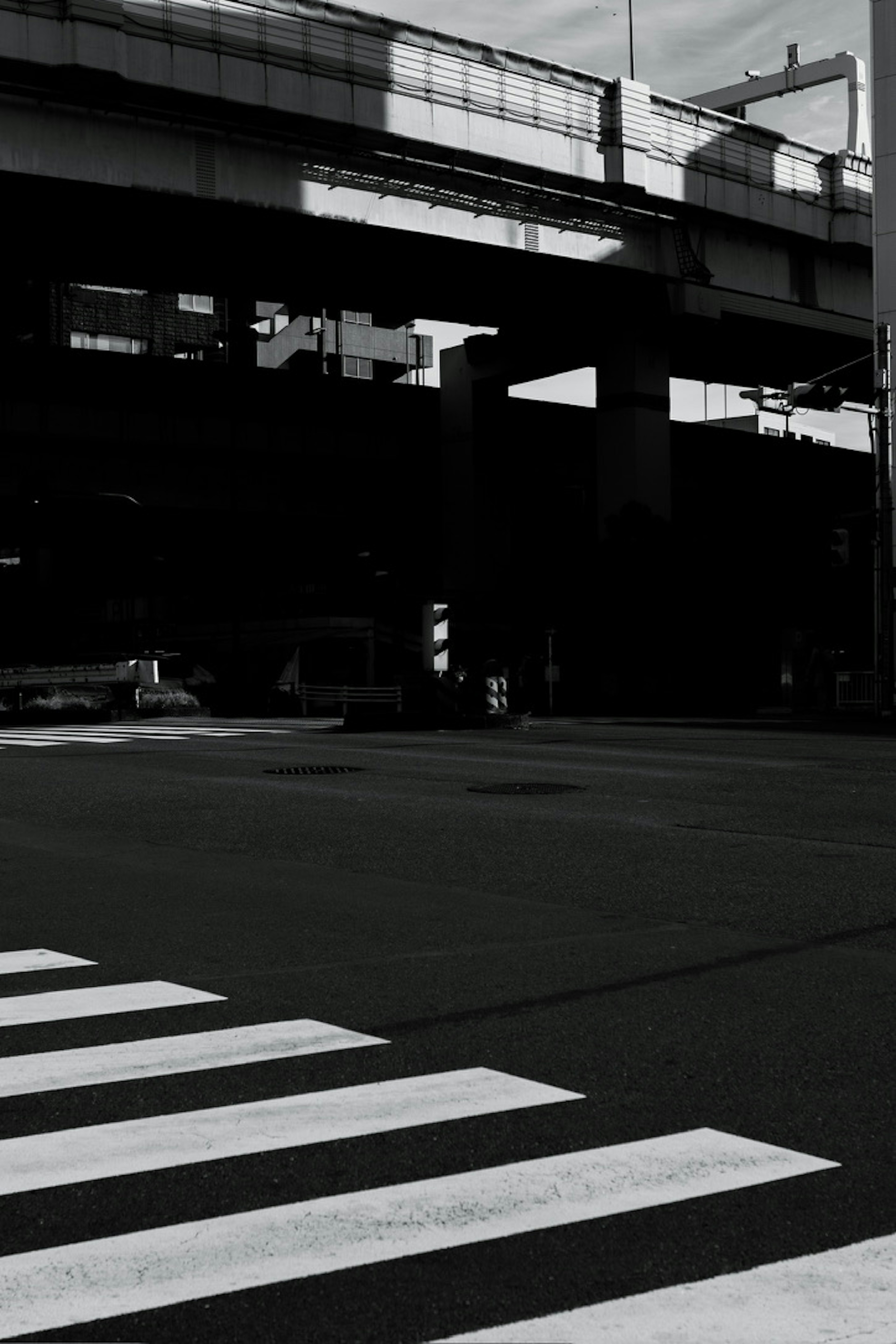 Black and white striped crosswalk with shadowed overpass in the background