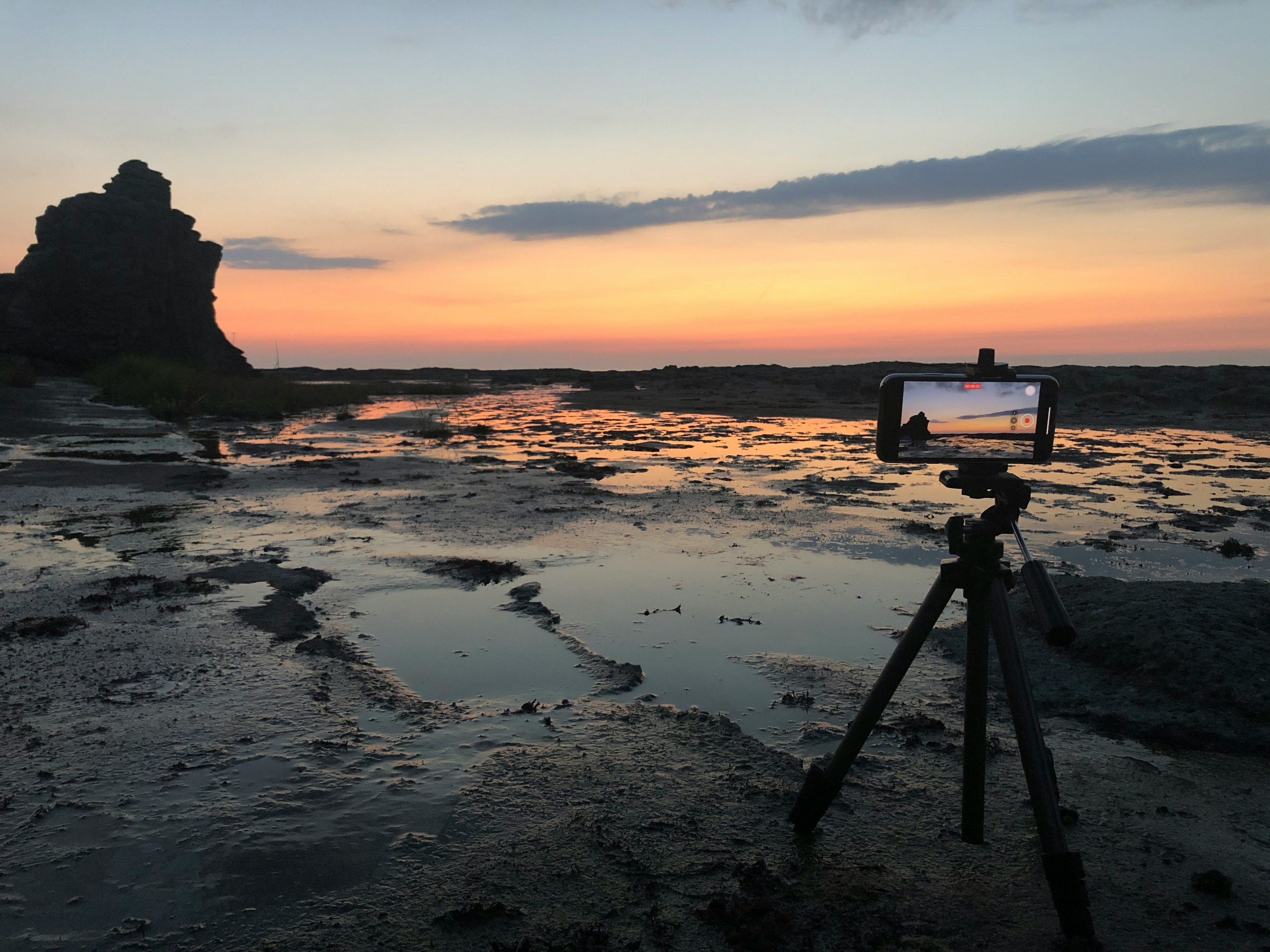 夕焼けの海岸で三脚に置かれたスマートフォンの風景