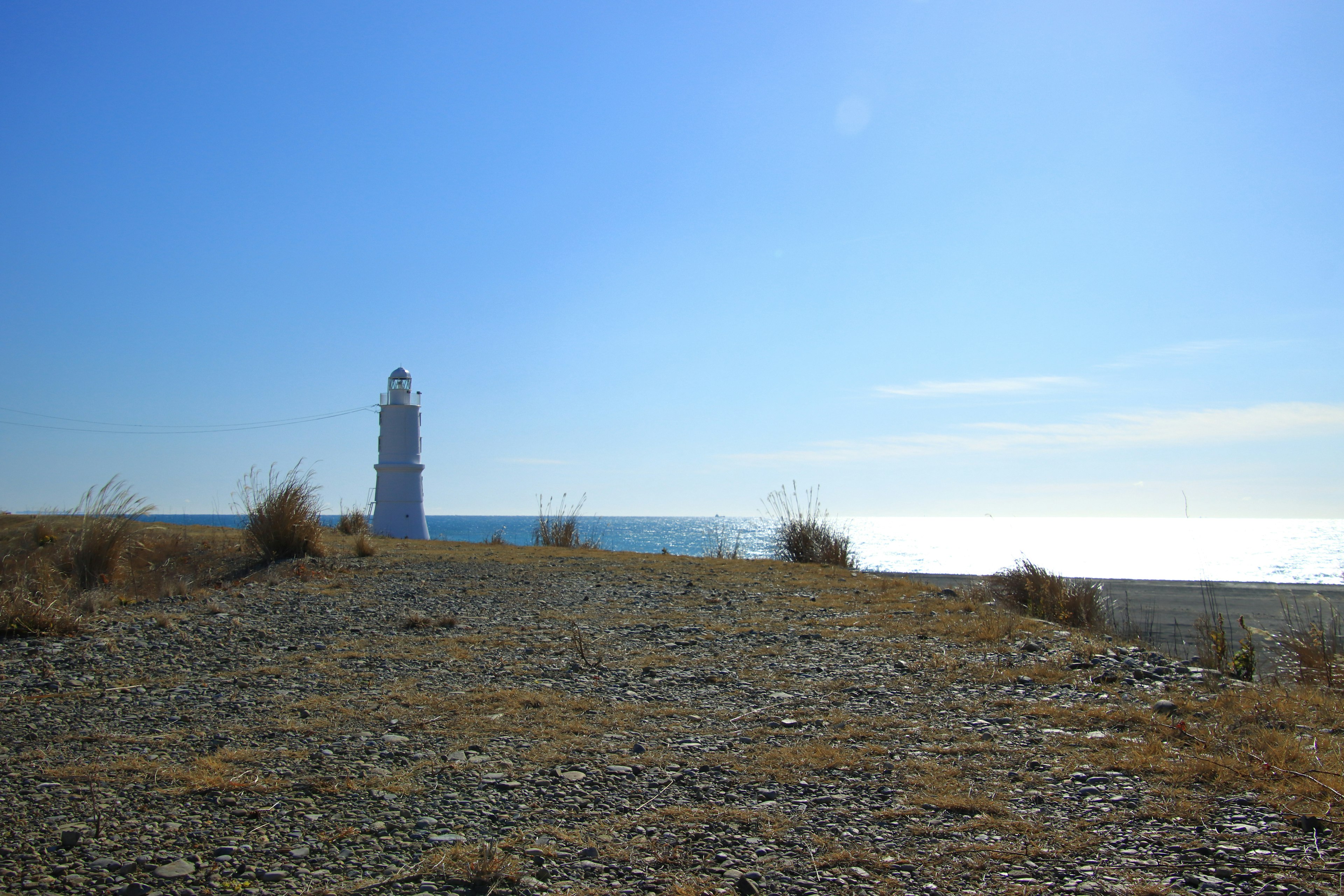 Ein Leuchtturm steht unter einem blauen Himmel mit ruhigem Meer