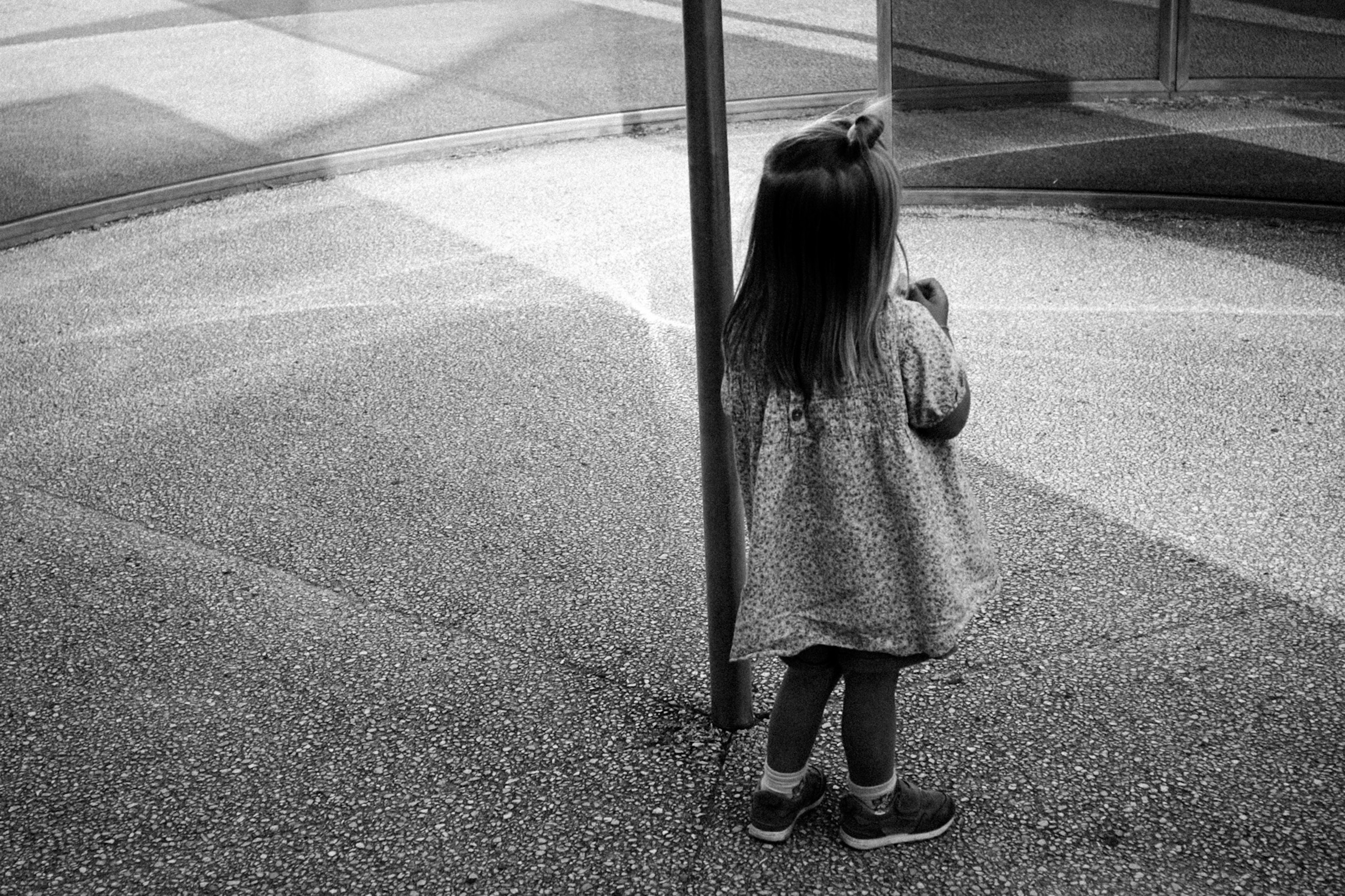 A young girl standing behind a pole in a black and white image