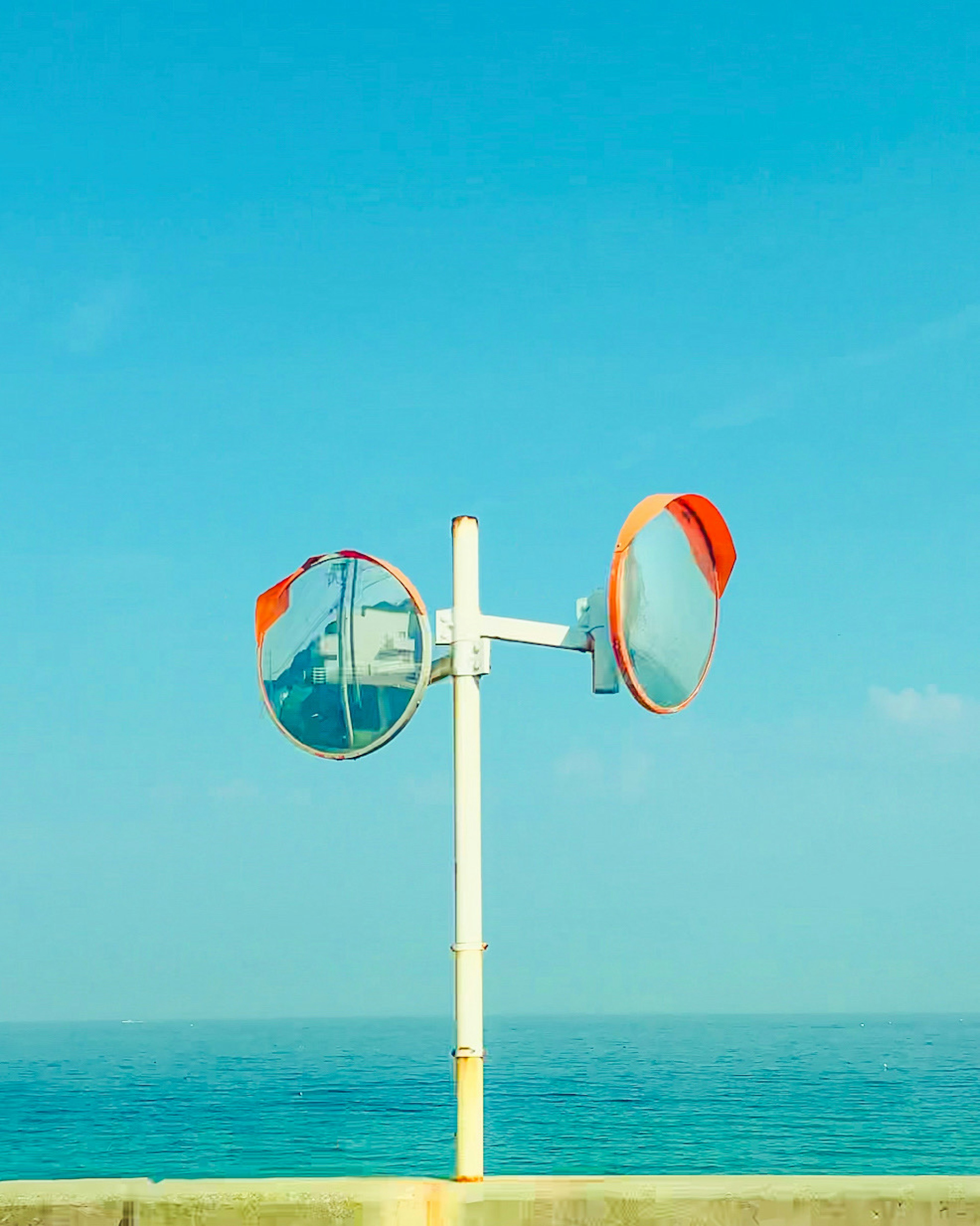 Two convex mirrors mounted on a pole against a blue sky and ocean