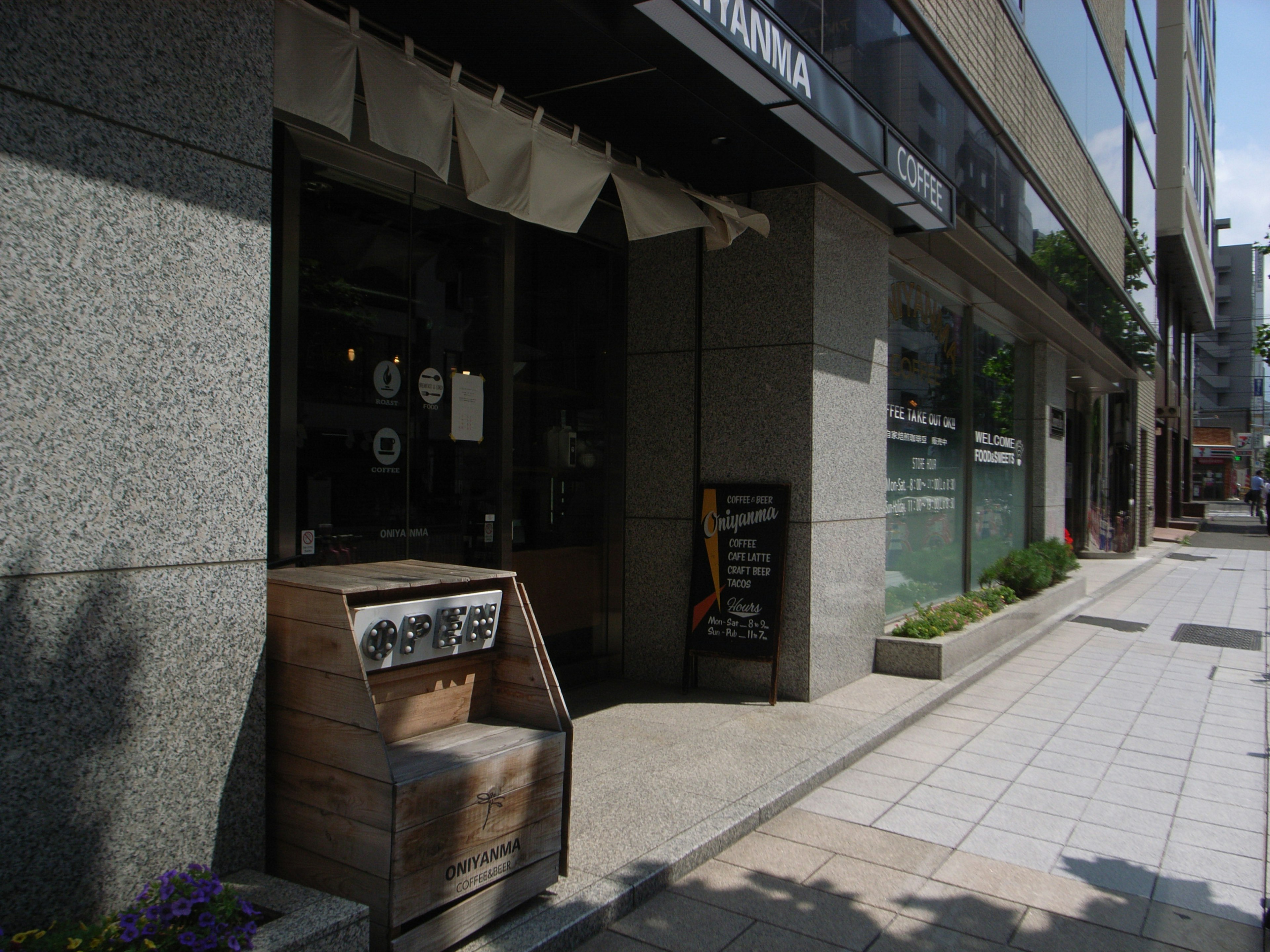 Exterior de café con cartel de madera y área de asientos con flores en macetas