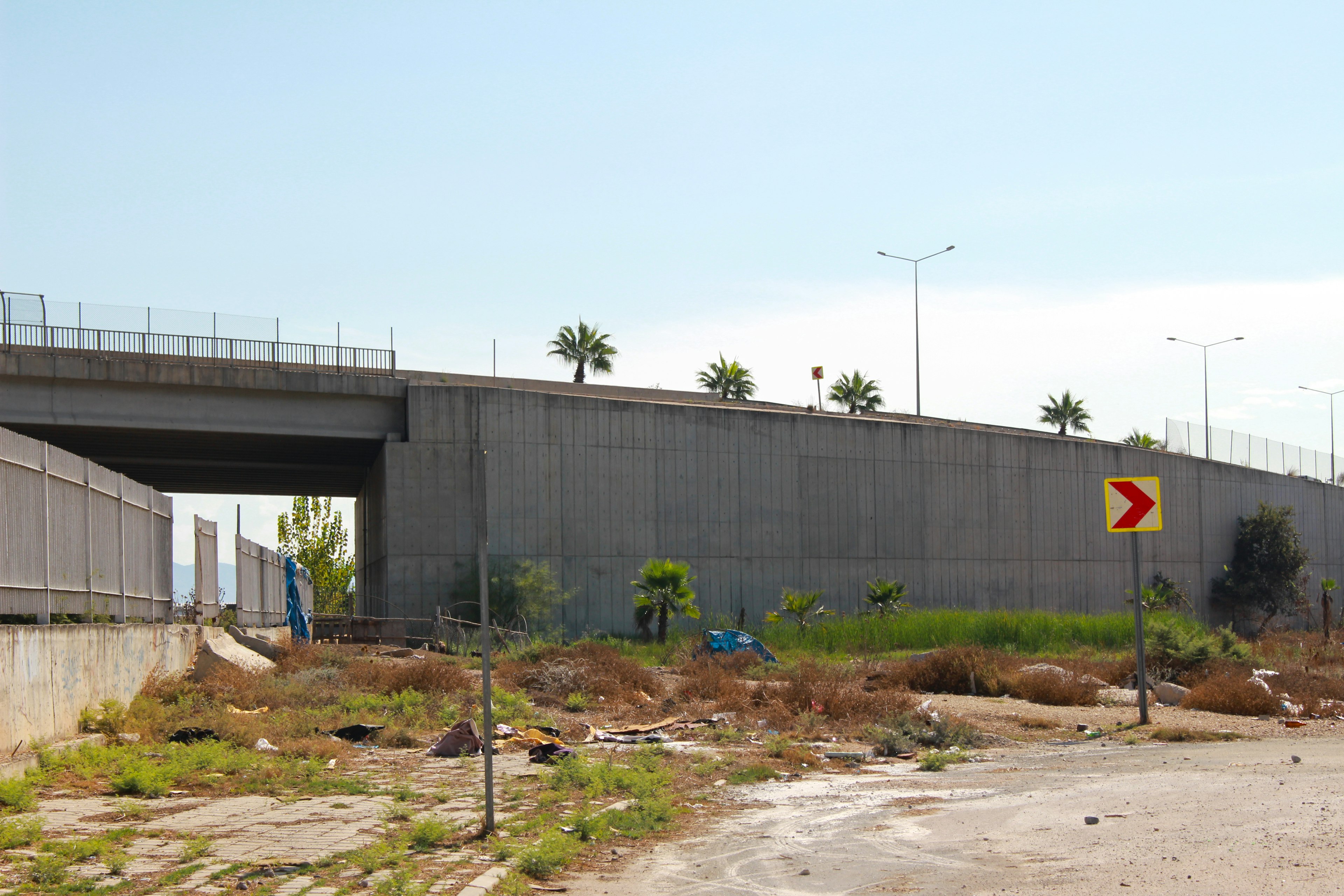 Paso elevado con terreno circundante cubierto de maleza y una señal de advertencia