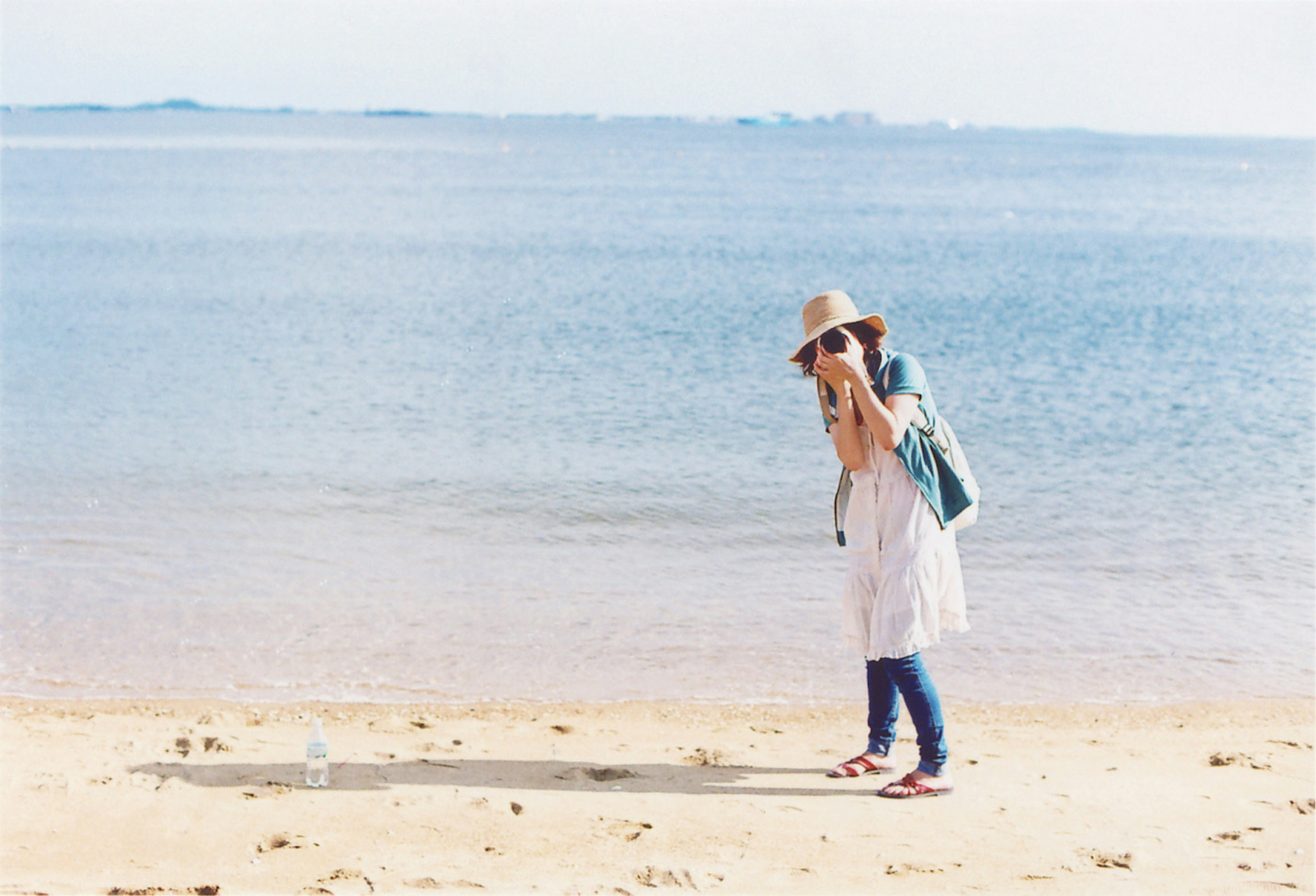 Femme marchant sur la plage portant une robe blanche et un chapeau avec un sac à dos