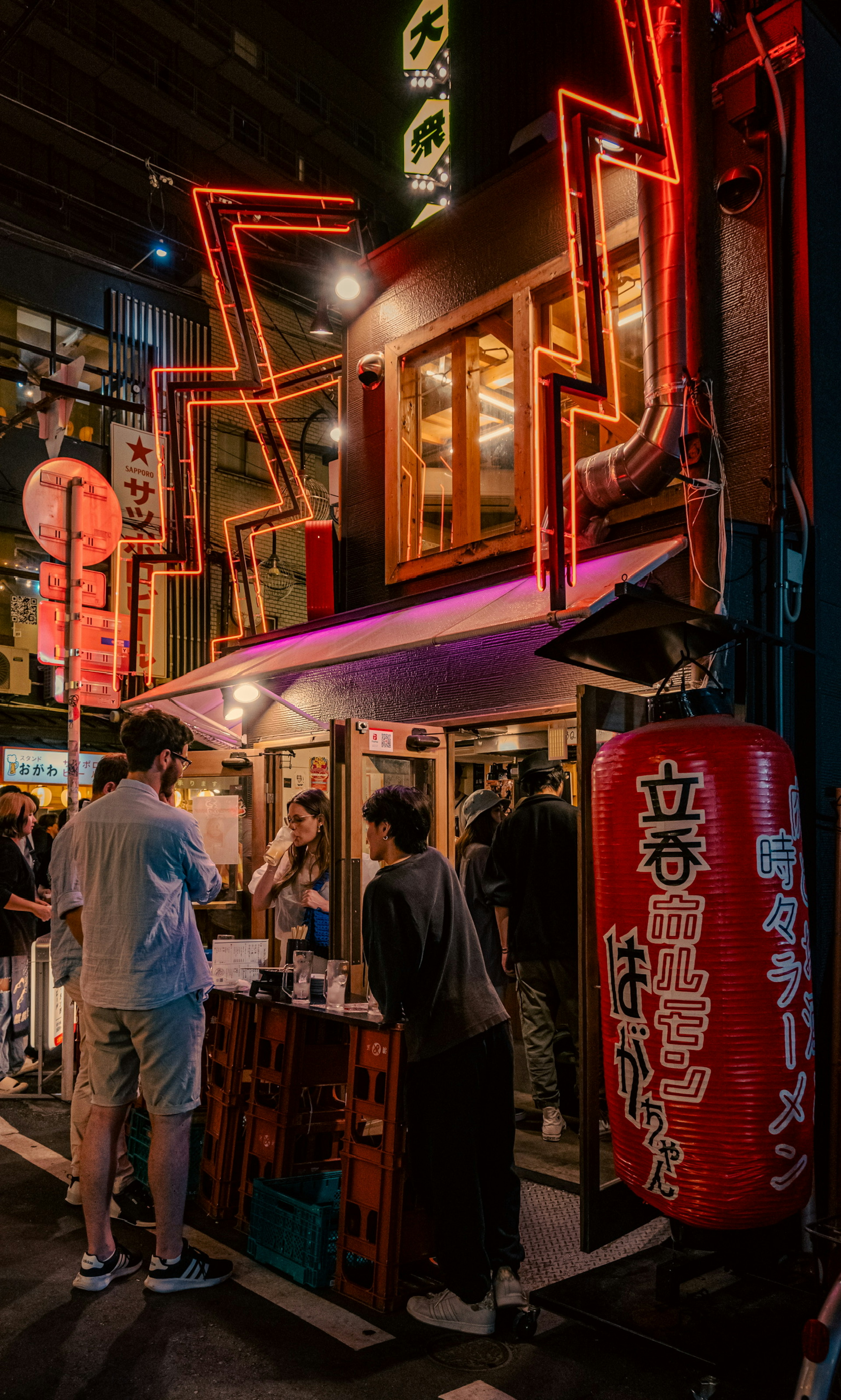 夜の街並みでネオンの看板が光る屋台の前に立つ人々