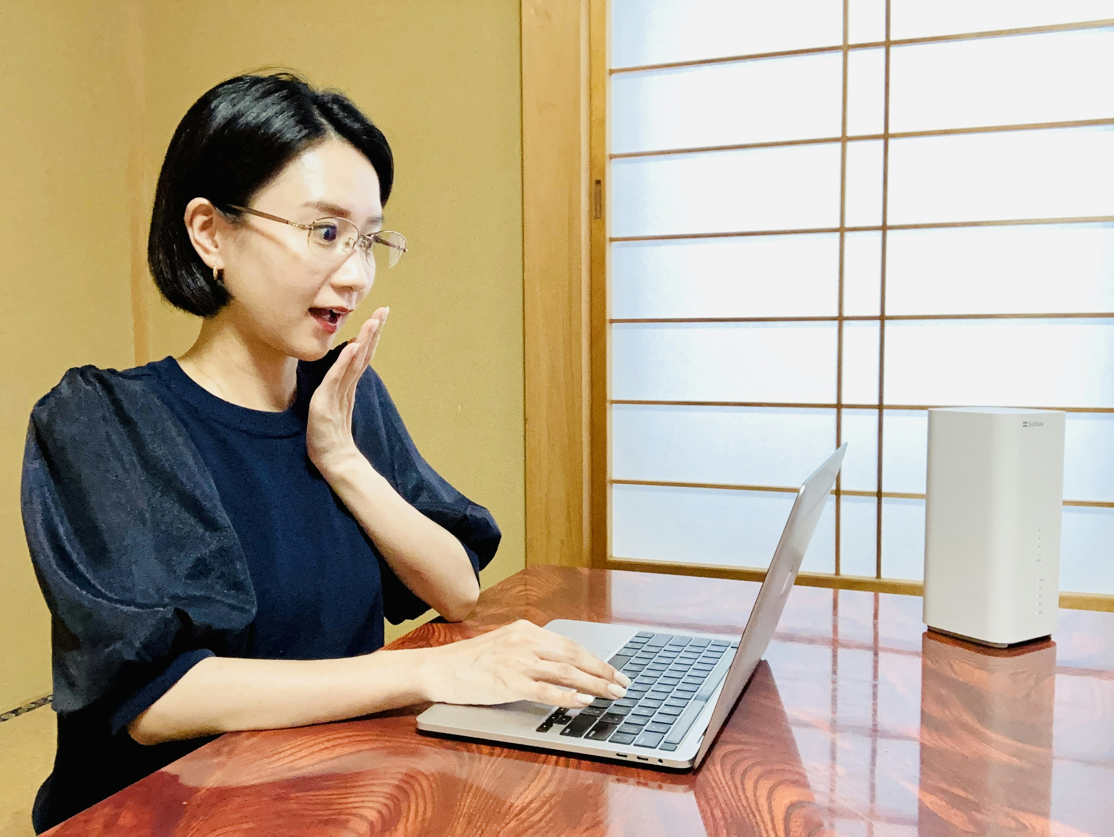 여성이 전통 일본 방에서 노트북을 사용하며 놀란 표정을 짓고 있다