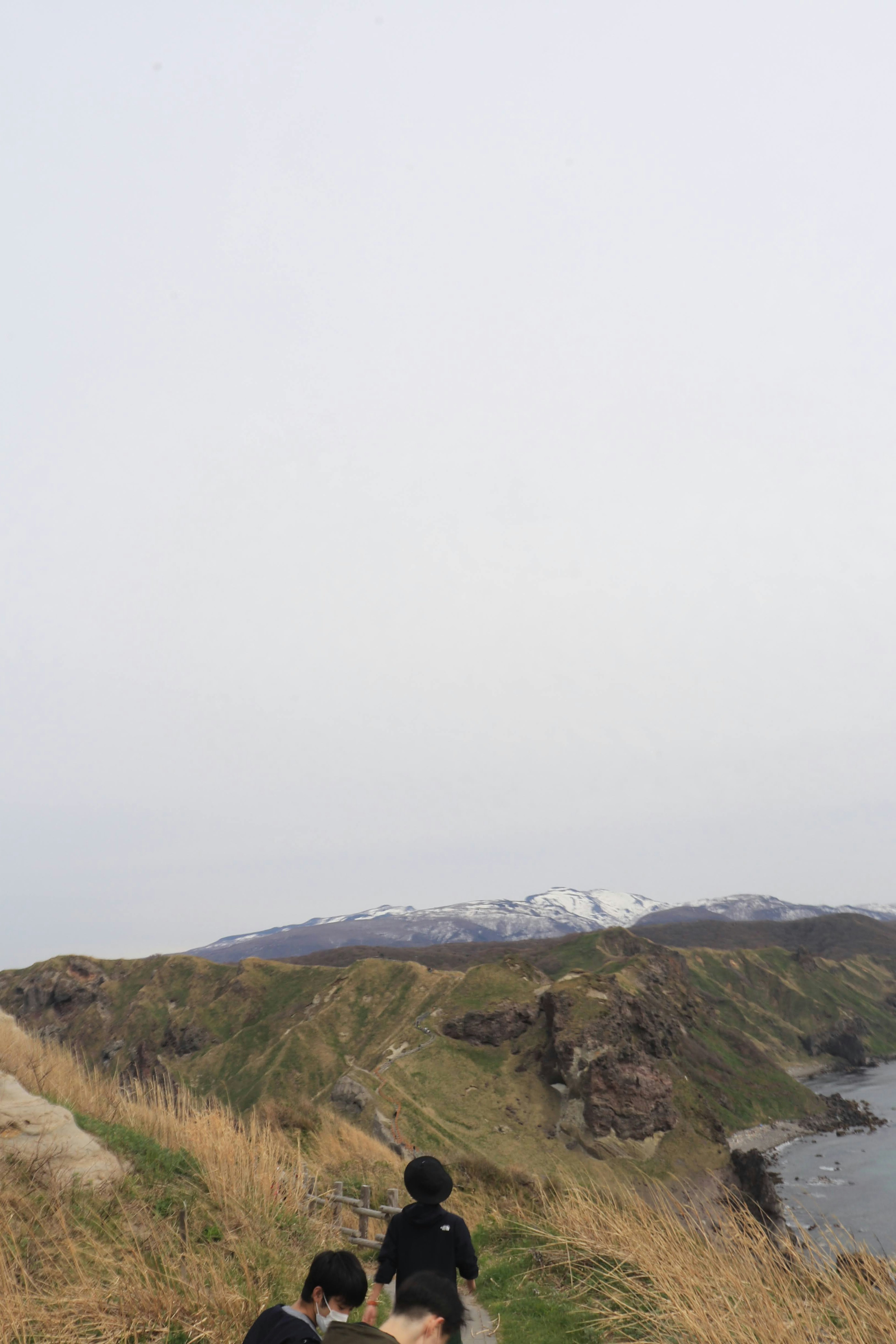 People walking along a coastal cliff with snow-capped mountains in the background