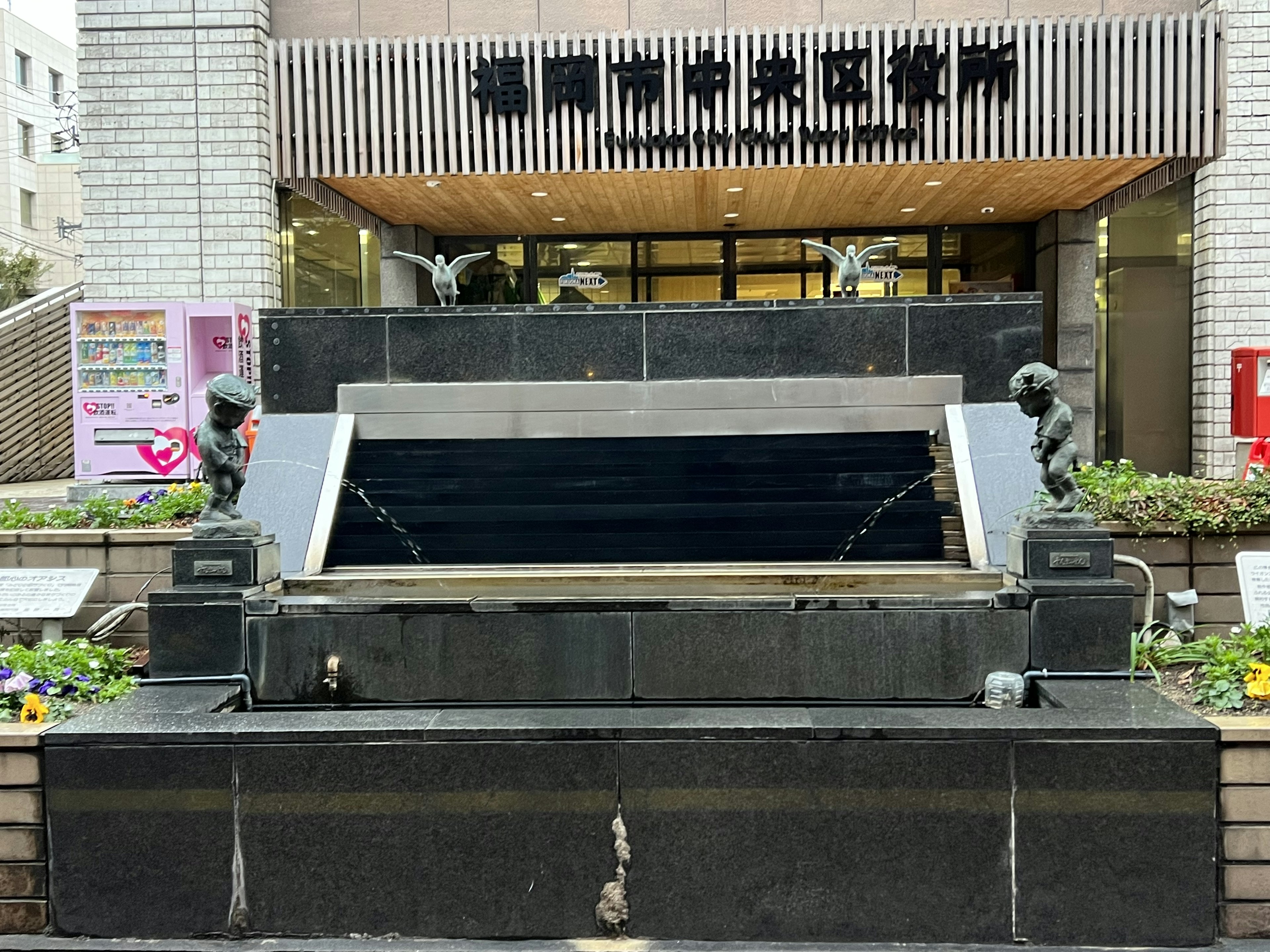 Black stone fountain with two statues in front of a building