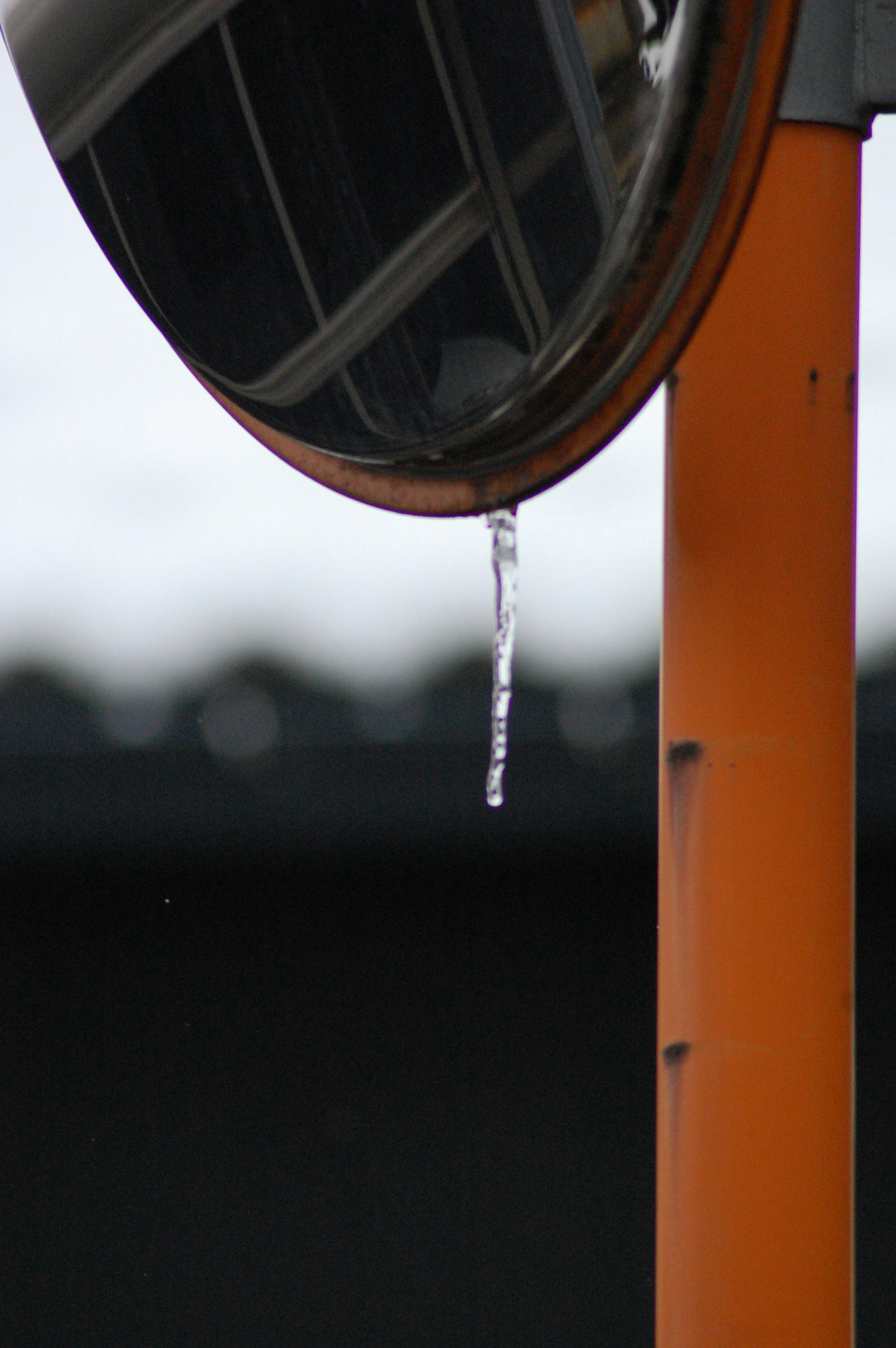 Una foto de un espejo adjunto a un poste naranja con una gota de agua colgando de él