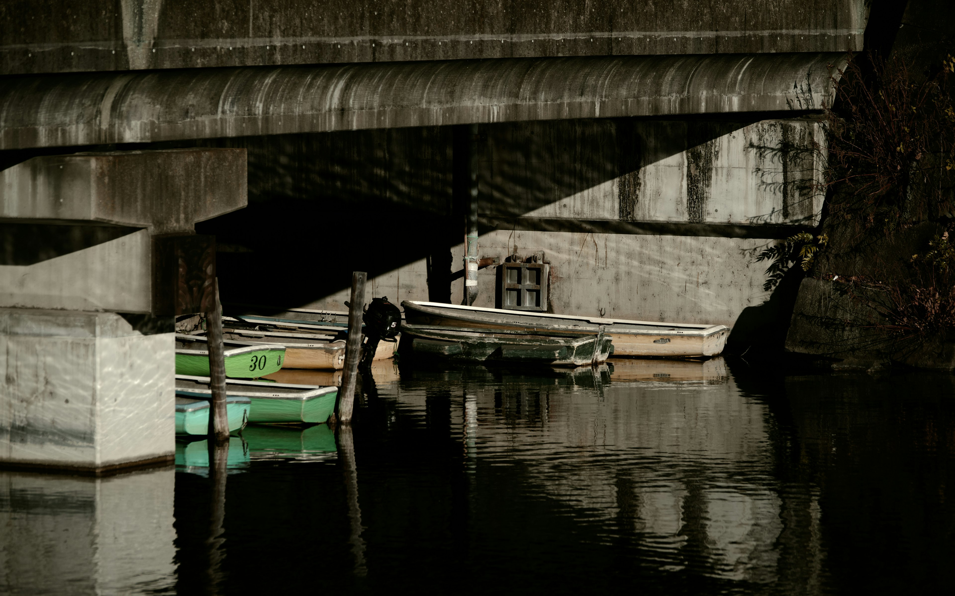 Petits bateaux amarrés sous un pont avec des reflets sur l'eau